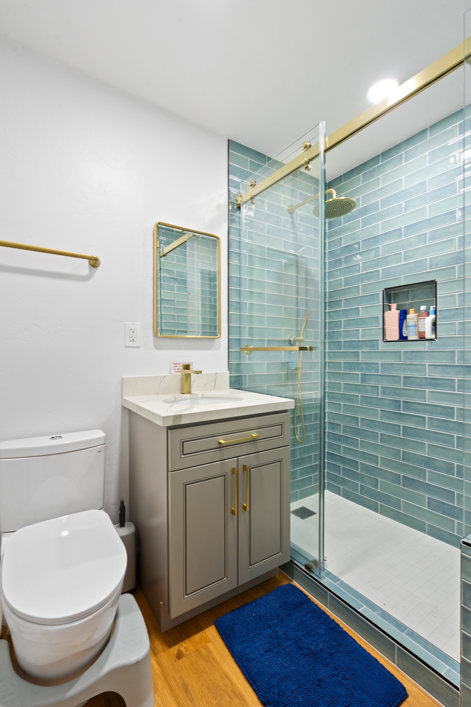 Bathroom with aqua glass tile shower, gold fixtures, and gray shaker vanity