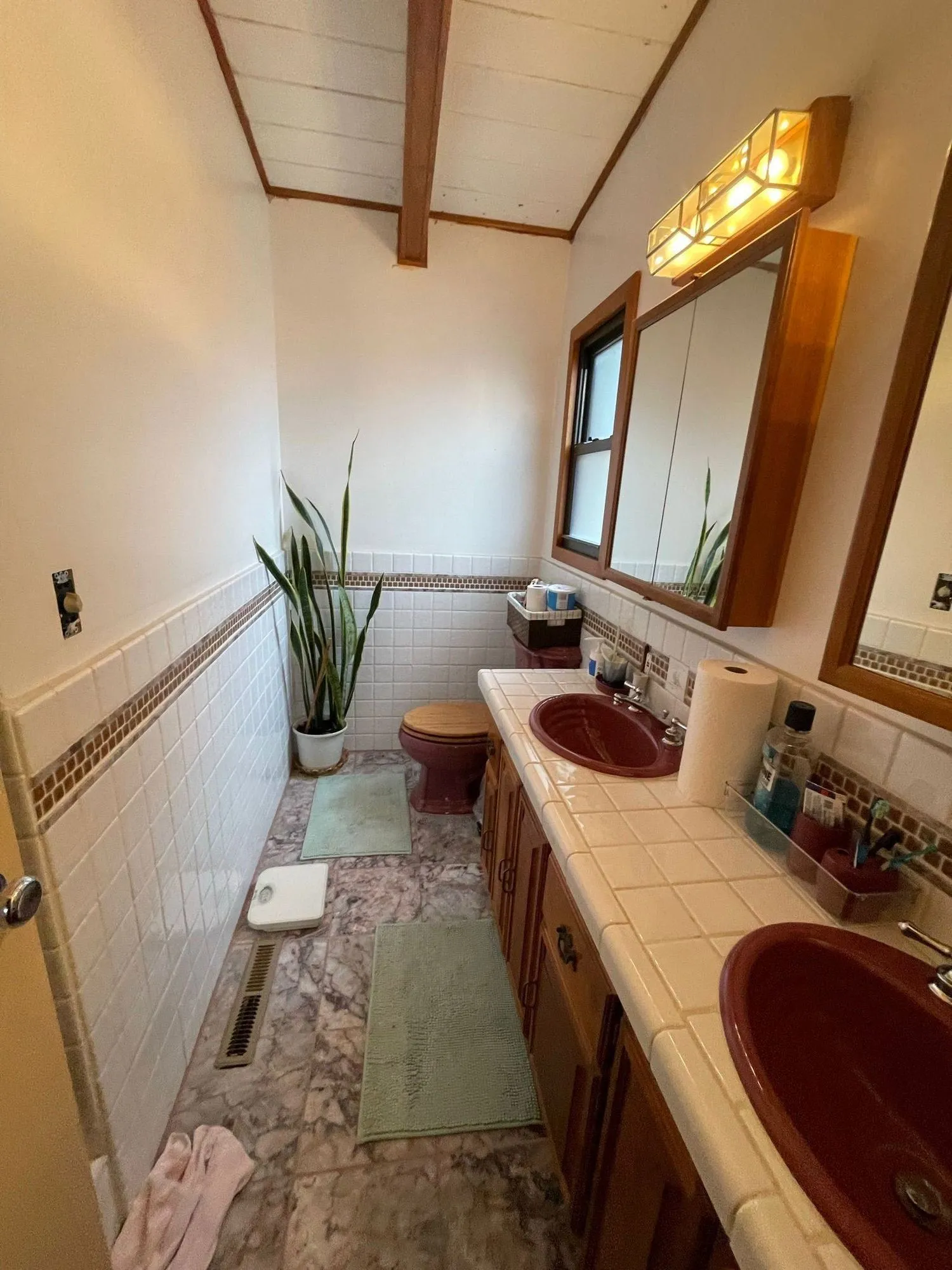 Original bathroom before remodel, tiled counter with two dark red drop-in basins and wood-framed medicine cabinets