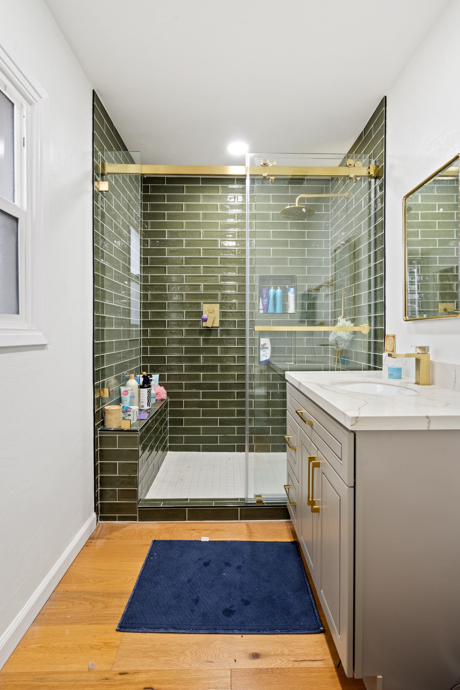 Bathroom with green subway tile shower, gold hardware, and gray shaker vanity