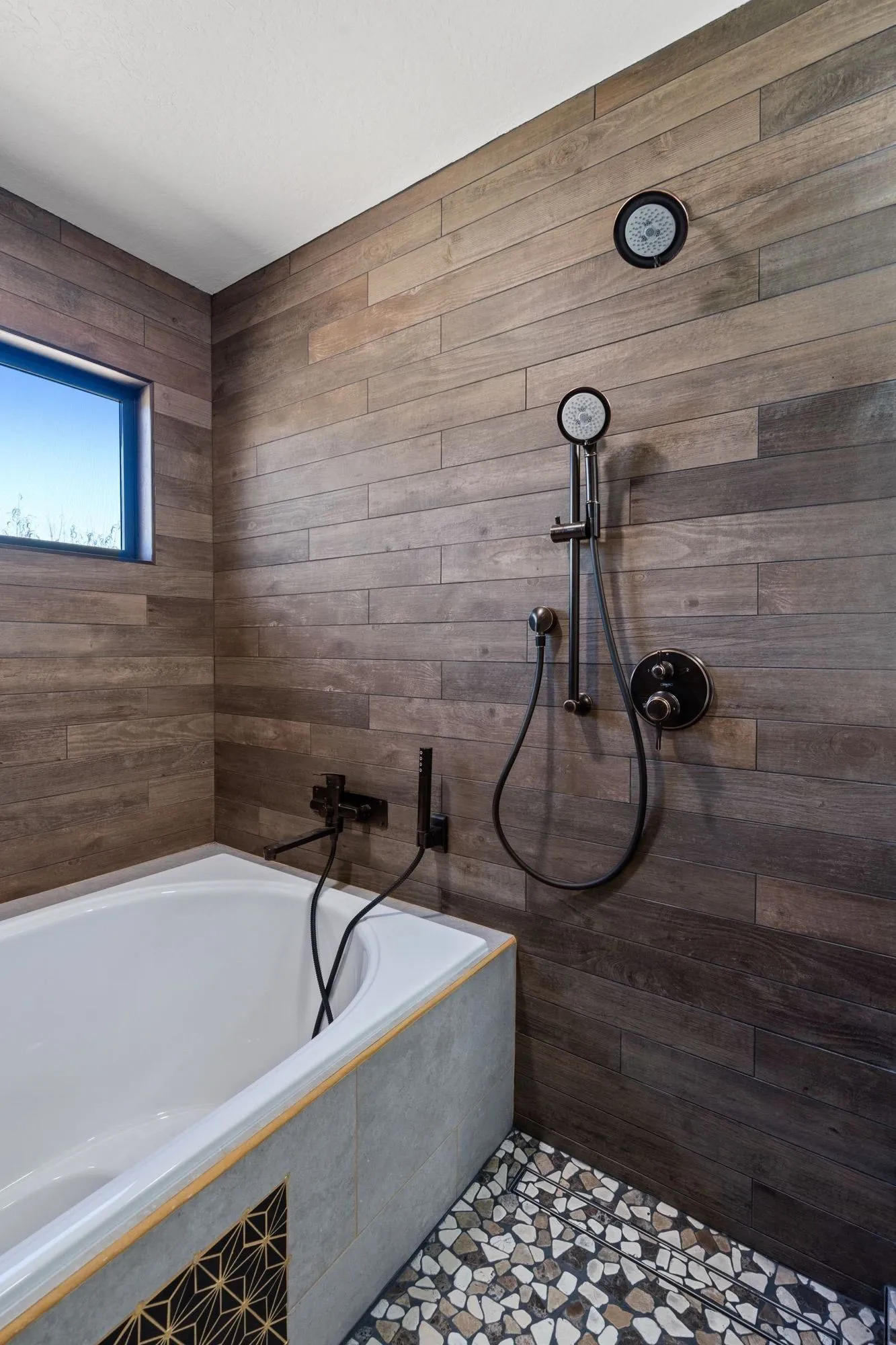 Shower fixtures on plank tile wall above pebble-mosaic floor