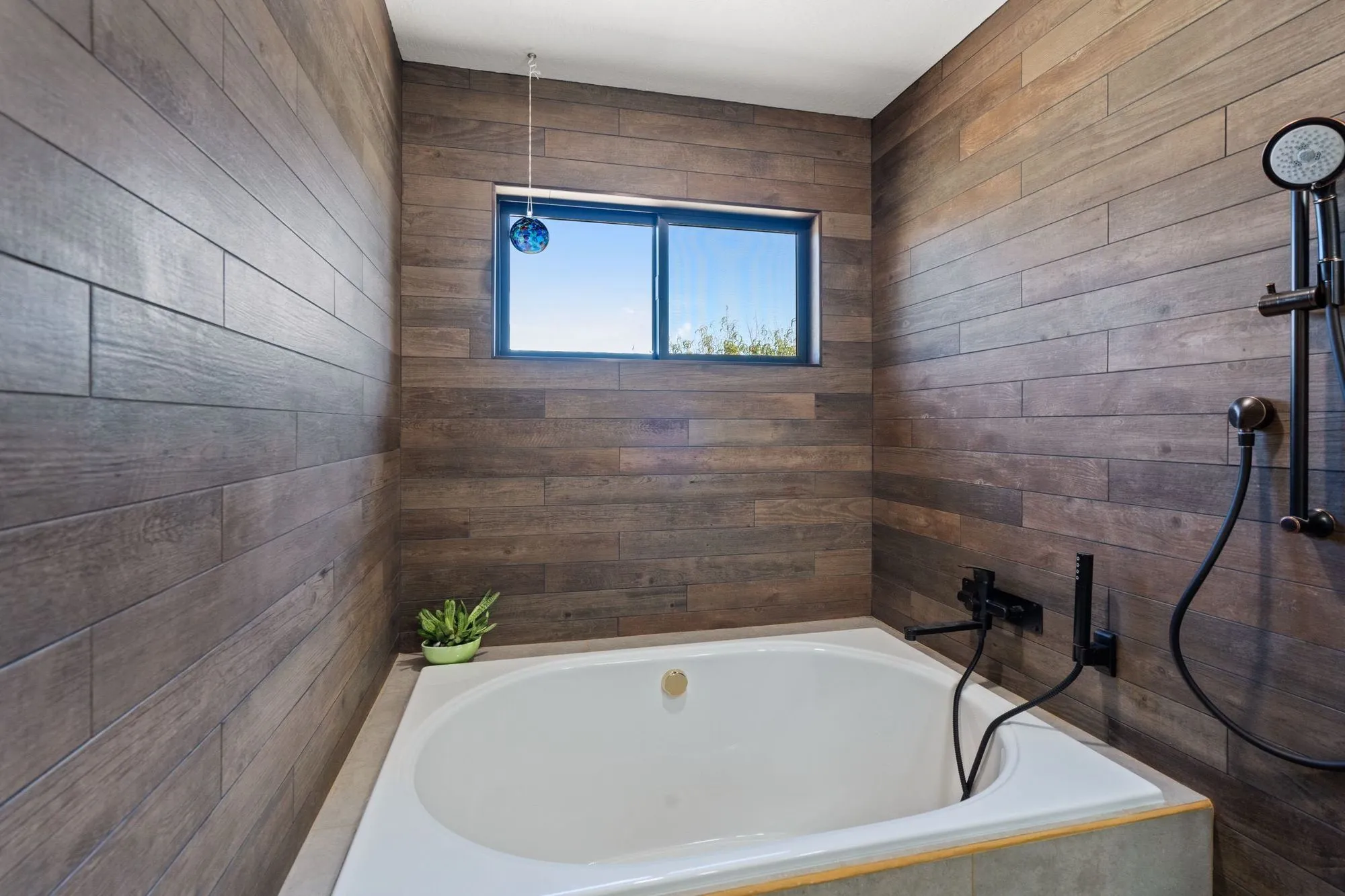 Drop-in soaking tub below a window, wood-look plank tile surround