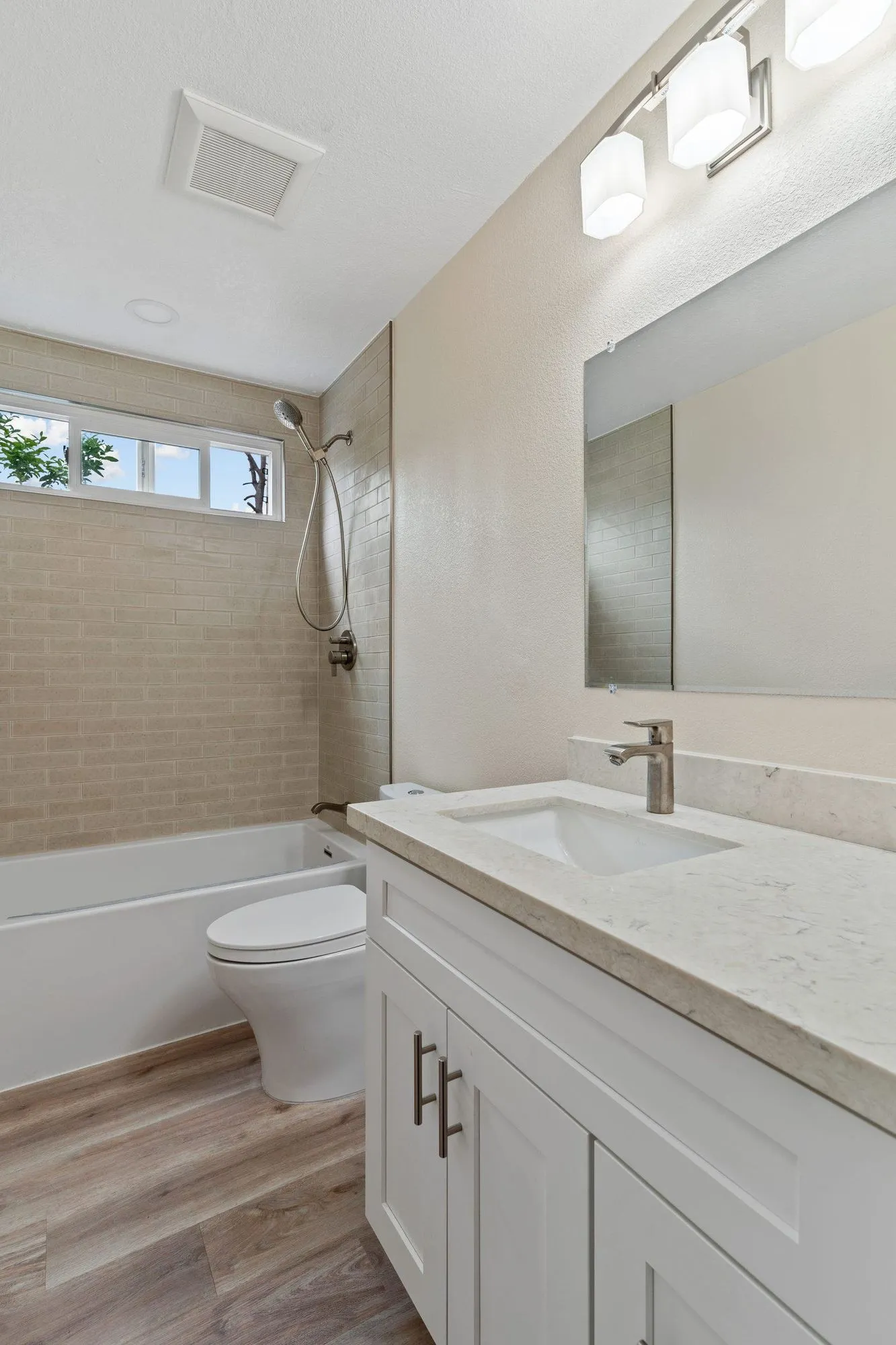 Bathroom after remodel, alcove tub with tile surround beside a white shaker vanity and quartz top