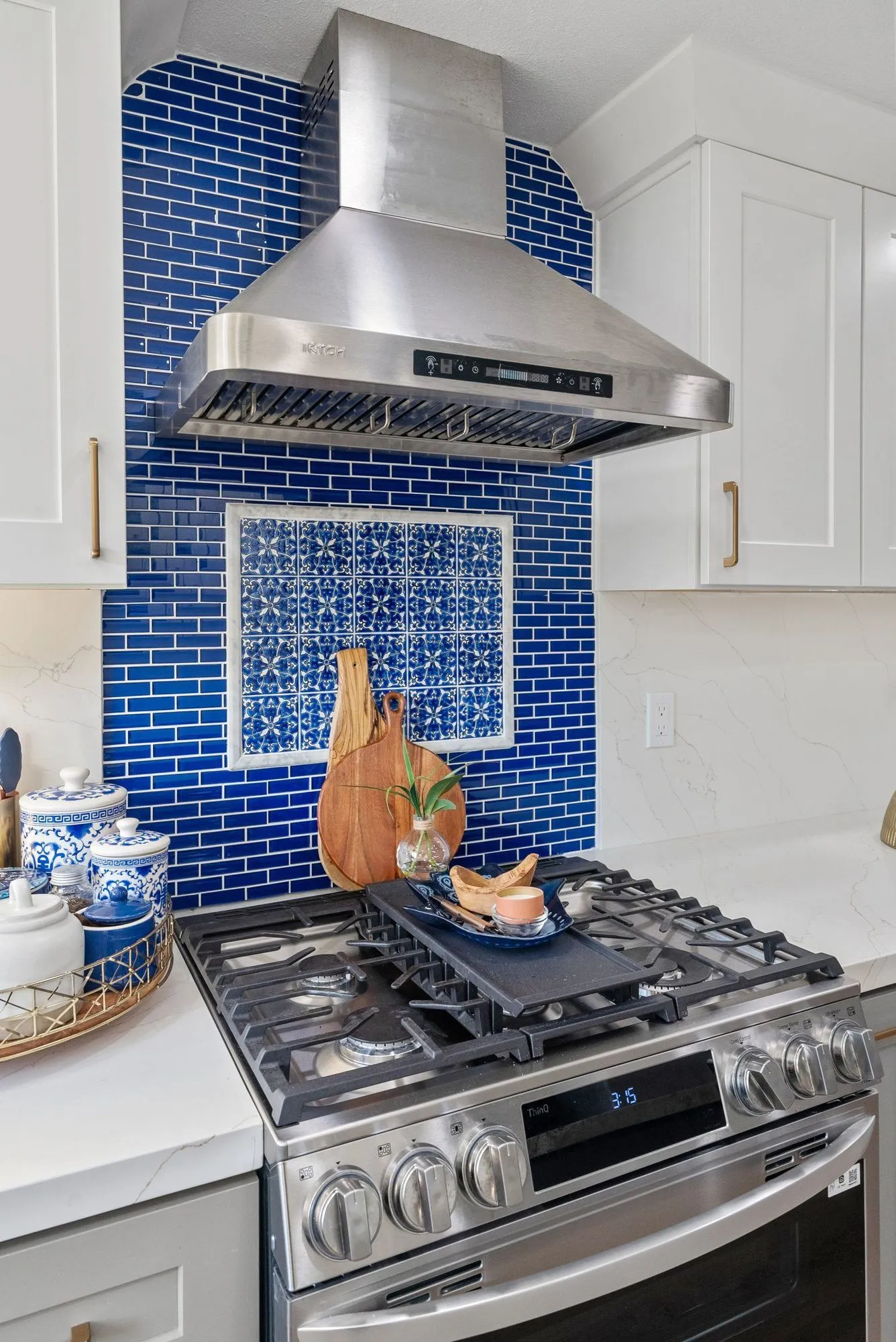 Stainless range below a chimney hood against the cobalt glass tile backsplash