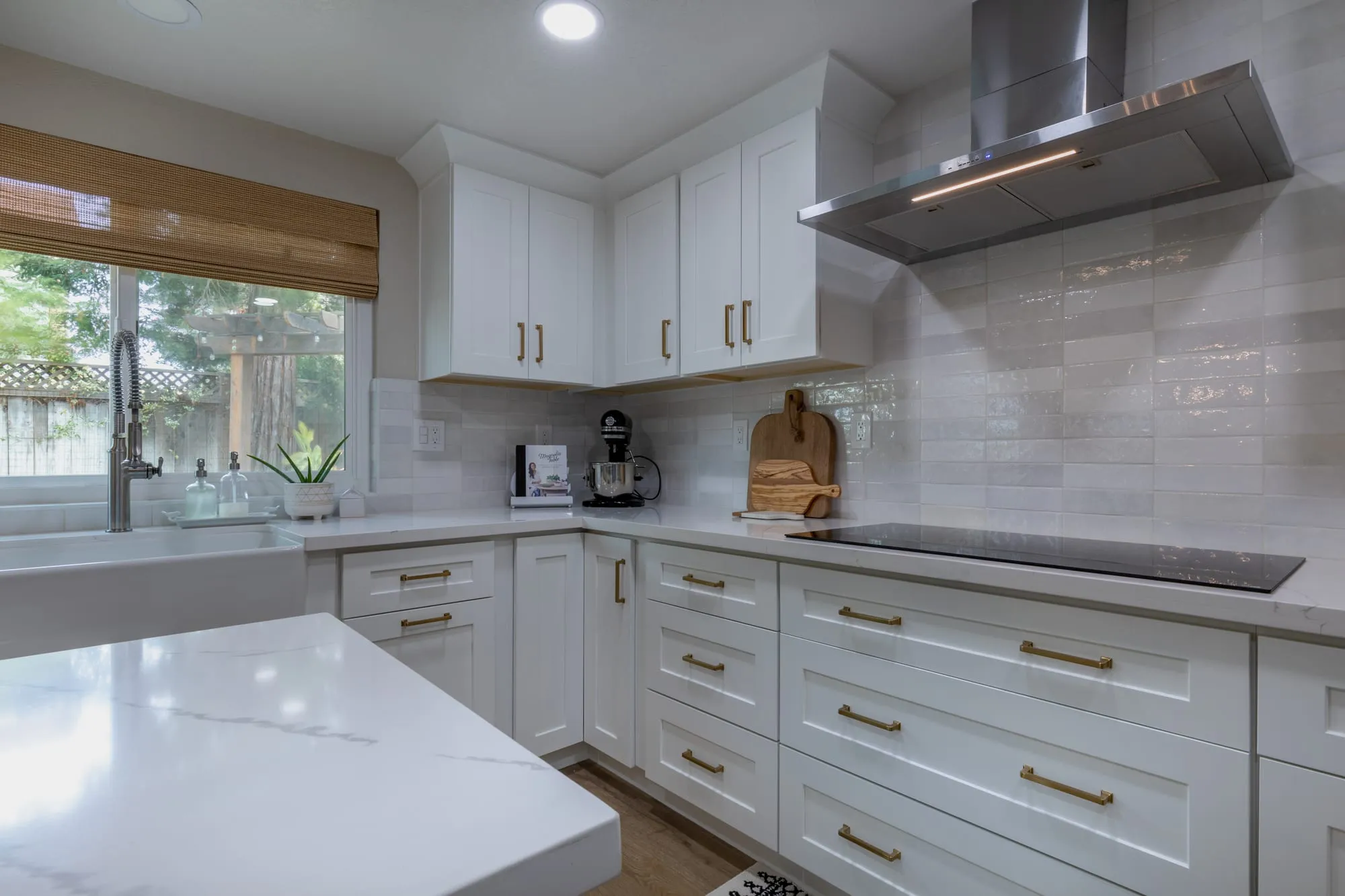 Cooktop under a stainless chimney hood in the corner of the quartz run