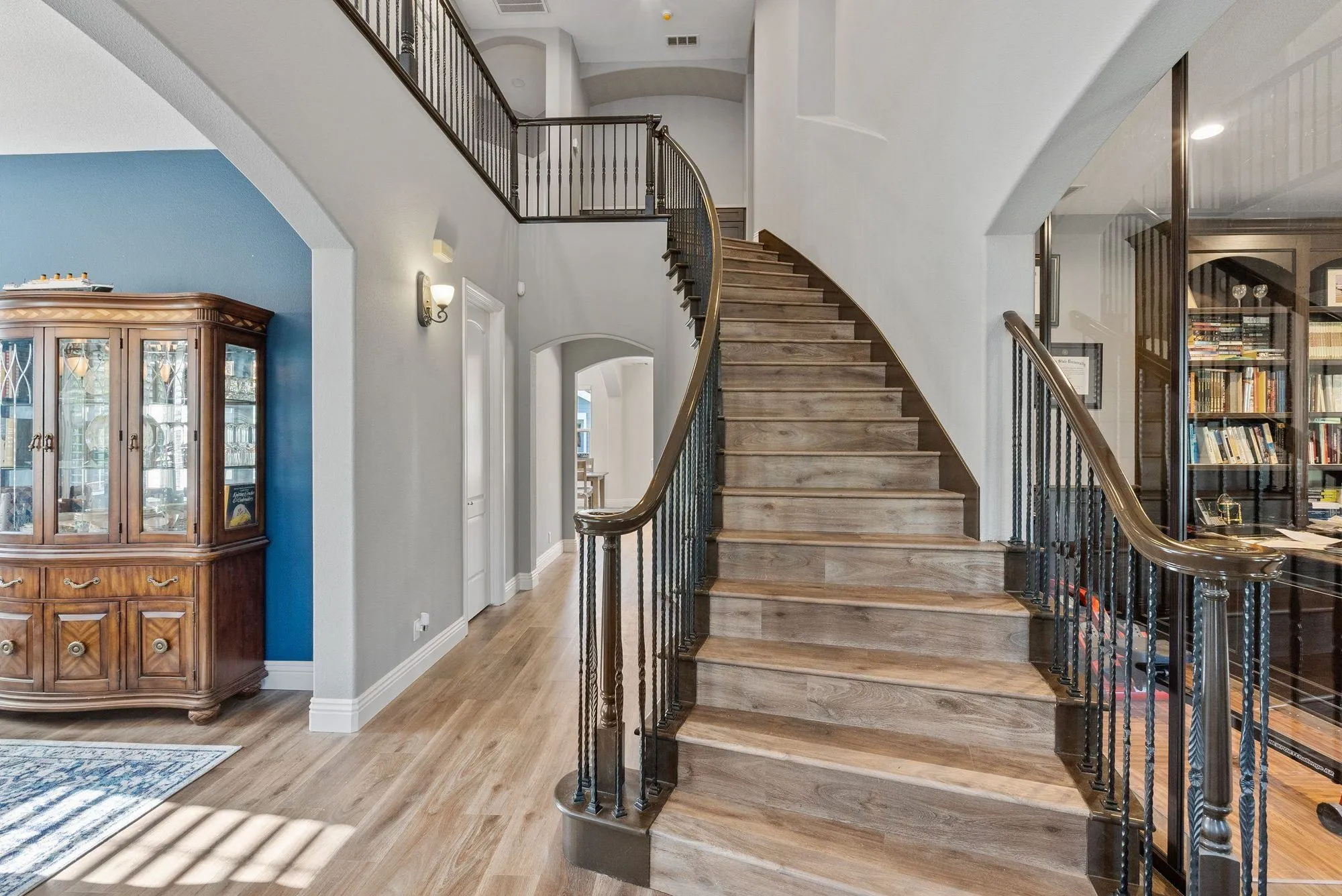 Staircase after remodel, curved run with slim black iron balusters and a plank-clad landing