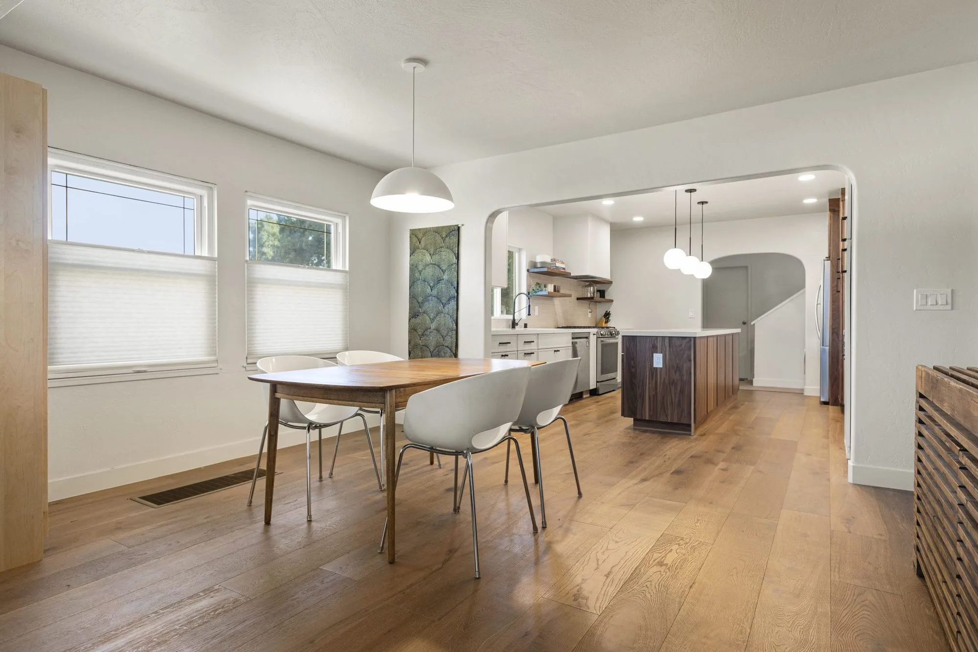 Dining table below a row of windows on wide-plank timber flooring