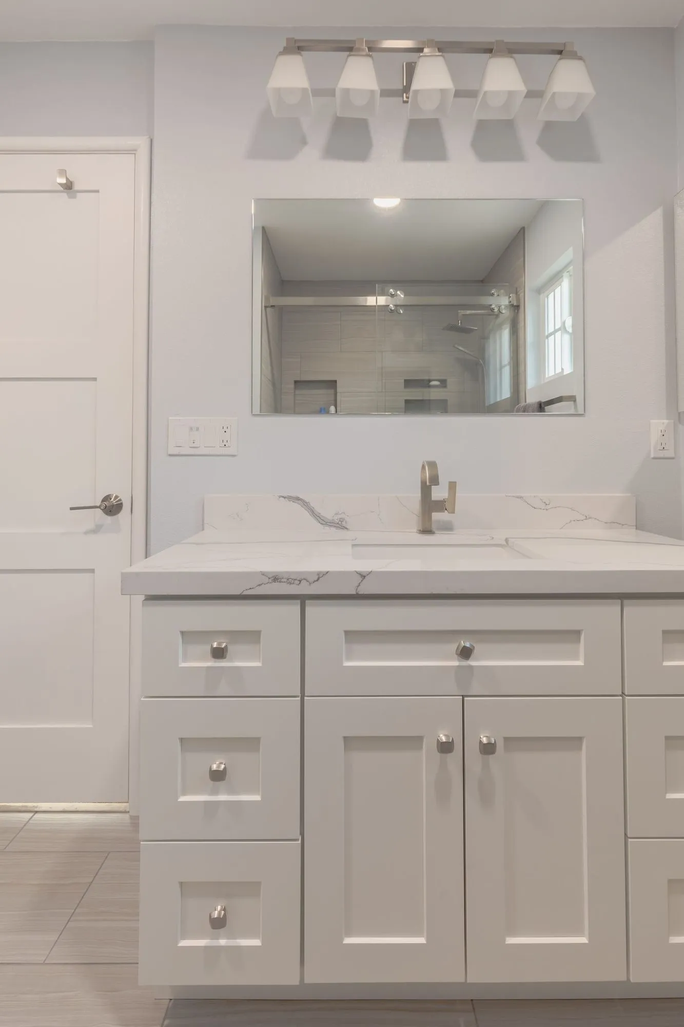 Double vanity in white shaker cabinetry with a quartz top and wide mirror