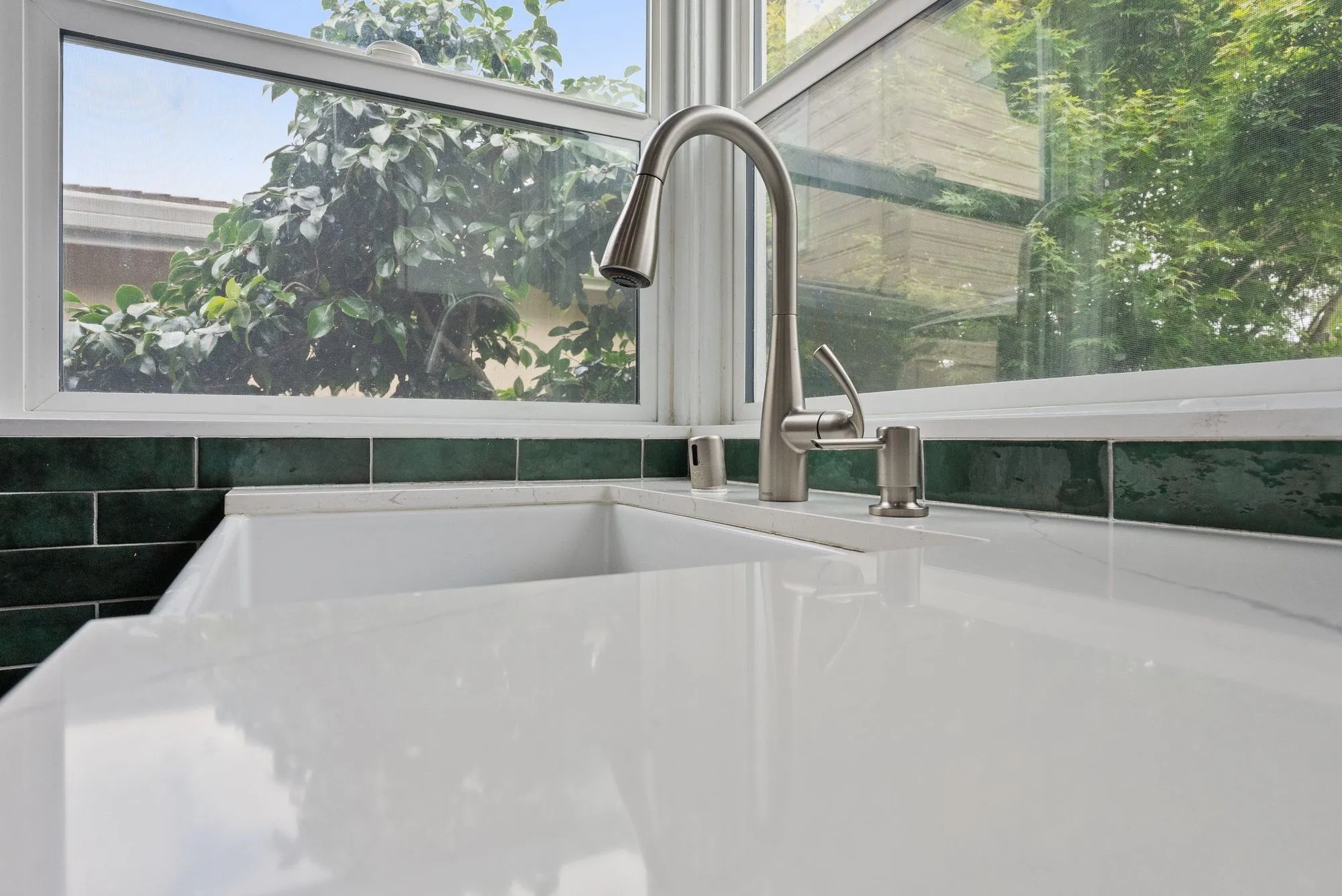 Close view of the apron-front farmhouse sink and pull-down tap against green tile