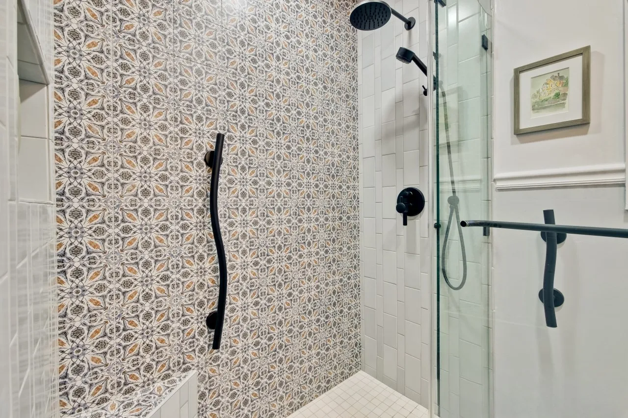 Patterned feature wall inside the shower beside stacked white tile with matte black rain head and hand shower