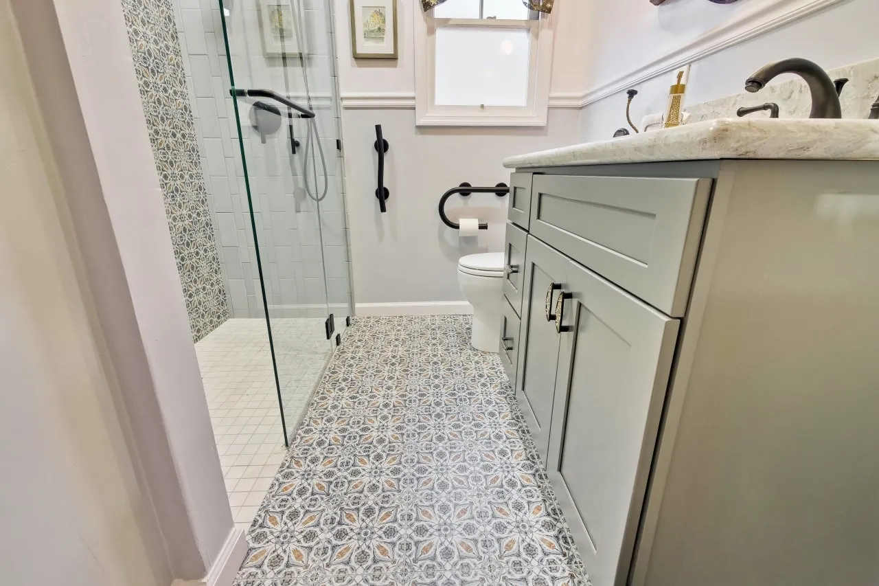 Patterned encaustic-look floor tile leading past the toilet toward the glass shower