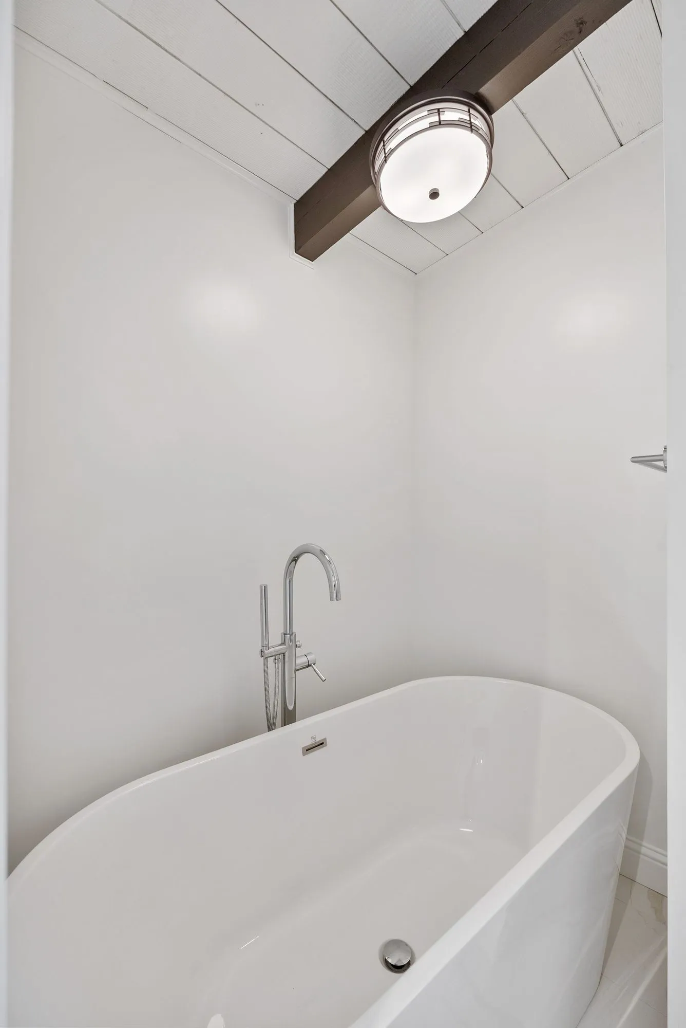 Freestanding tub below an exposed dark ceiling beam and shiplap ceiling