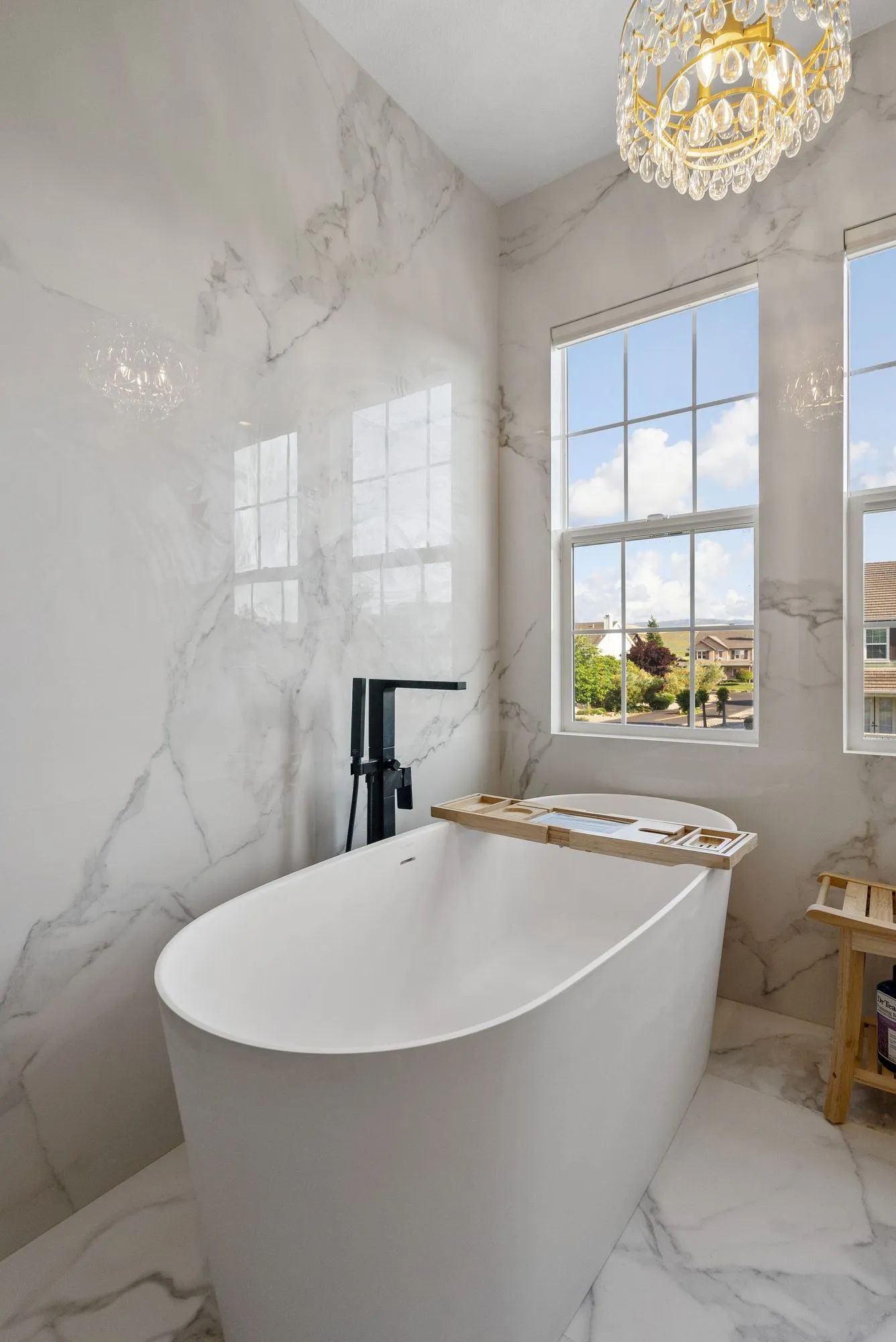 Freestanding soaking tub on marble-look tile below a small chandelier