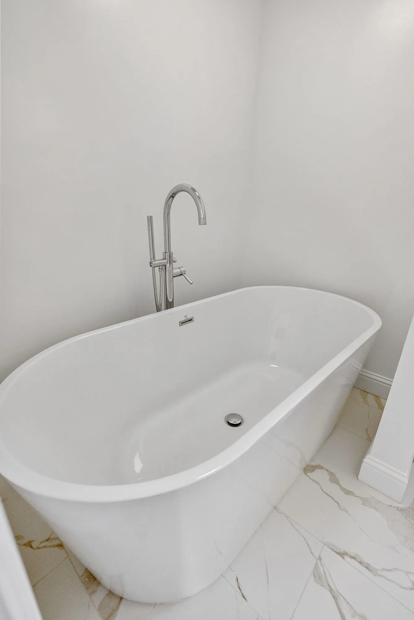 Freestanding soaking tub with floor-mounted filler on marble-look tile flooring