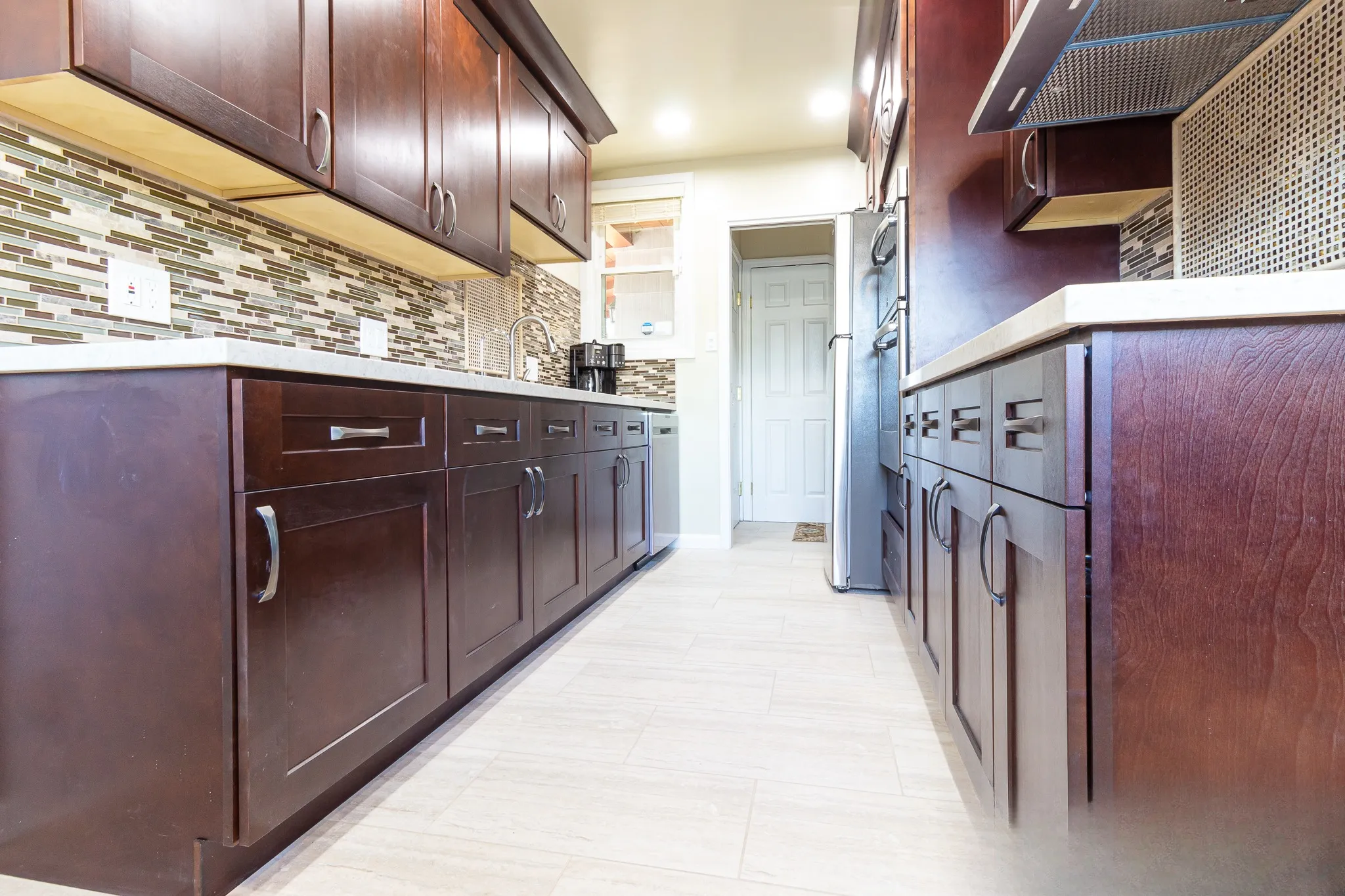 Galley kitchen looking along both cabinet runs toward a stainless refrigerator over light plank-look floor tile