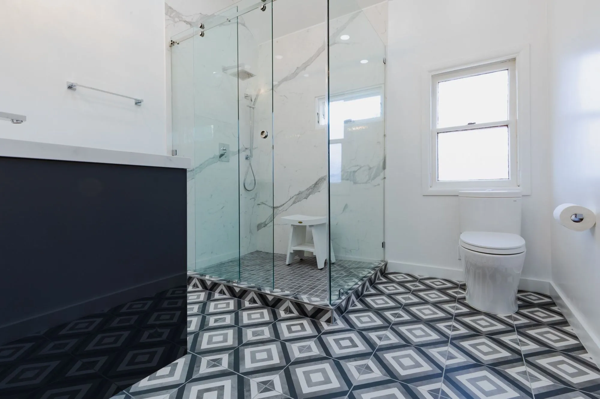 Frameless glass shower enclosure beside geometric black and white floor tile