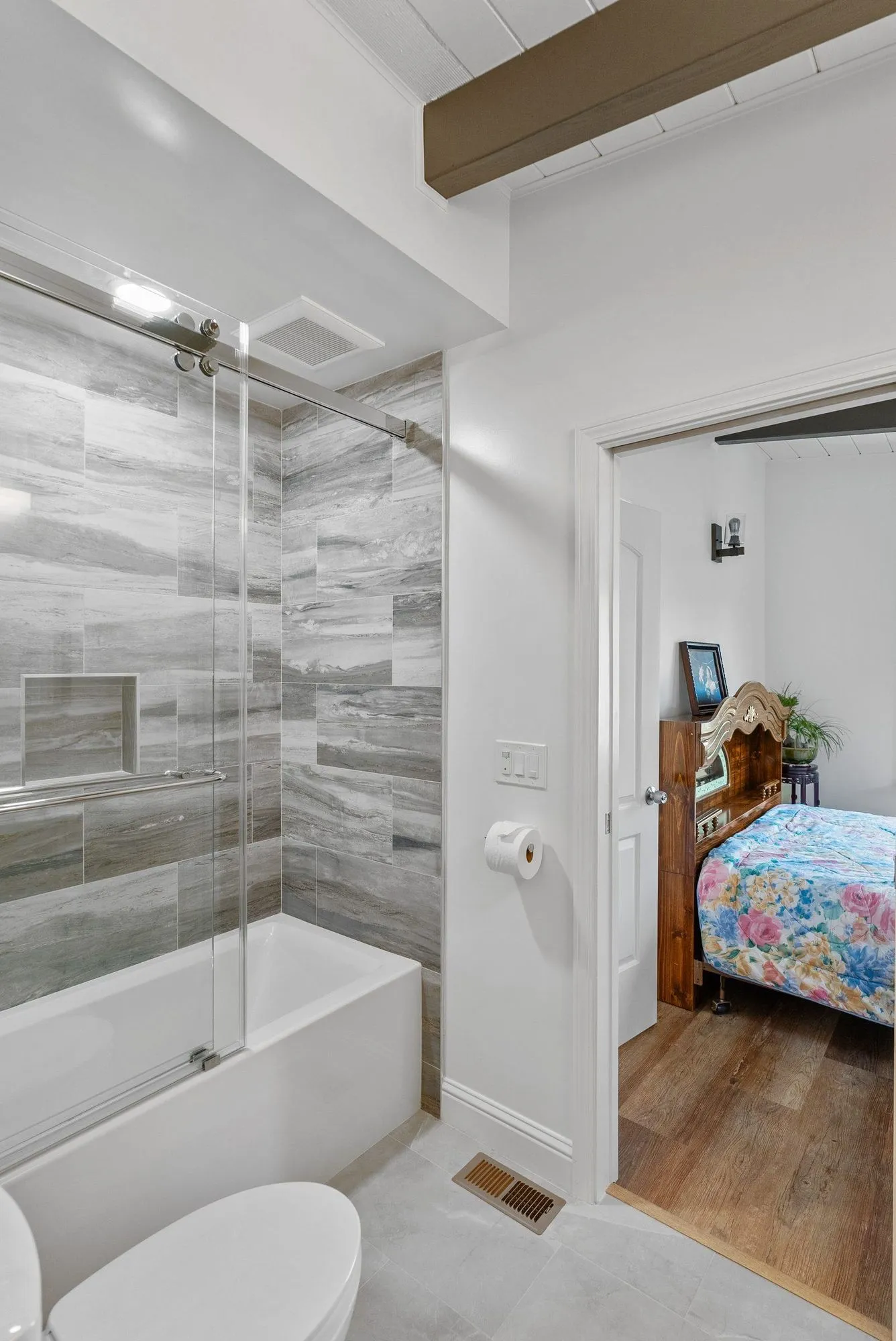 Tub and shower behind a glass panel, with the doorway open to a bedroom beyond
