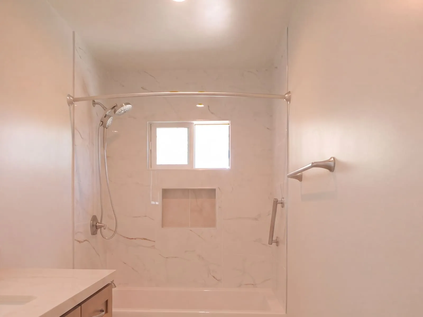 Hall bathroom after remodel, tub and shower lined in large-format marble-look tile with a recessed shampoo niche