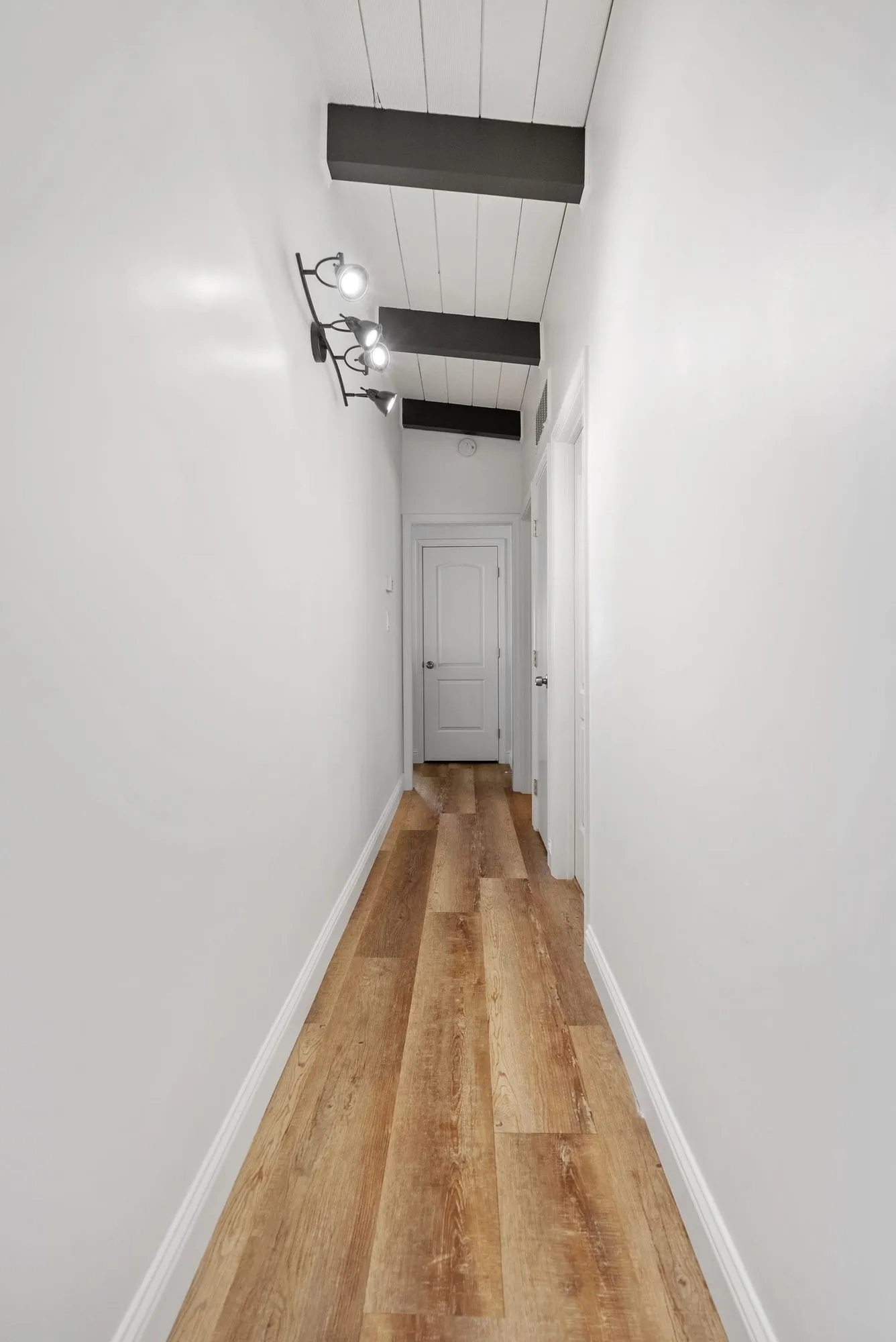 Hallway with light oak plank flooring, shiplap ceiling and an exposed dark beam