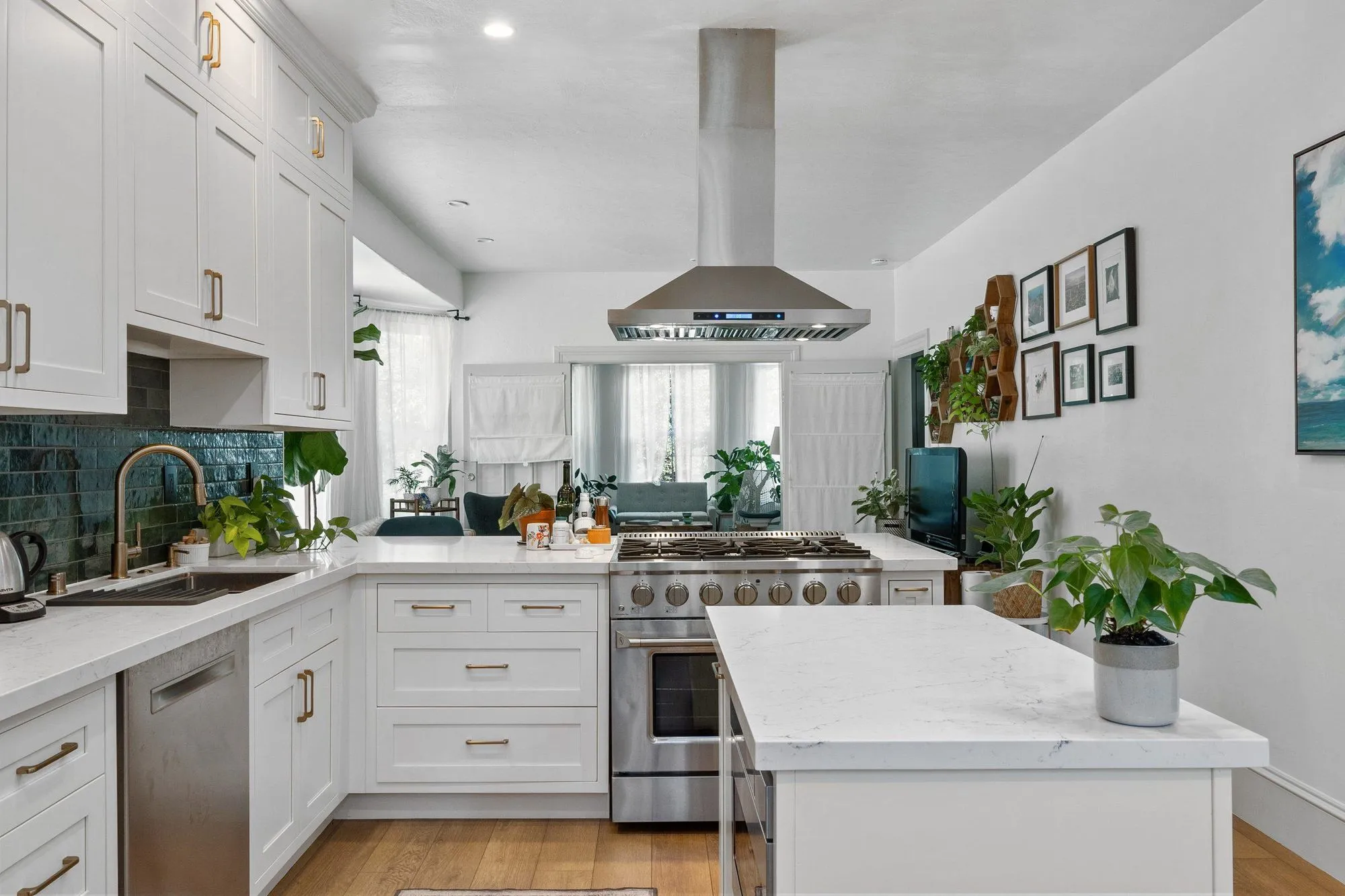 Kitchen after remodel, white shaker cabinetry against a deep teal backsplash with a quartz island below a stainless hood