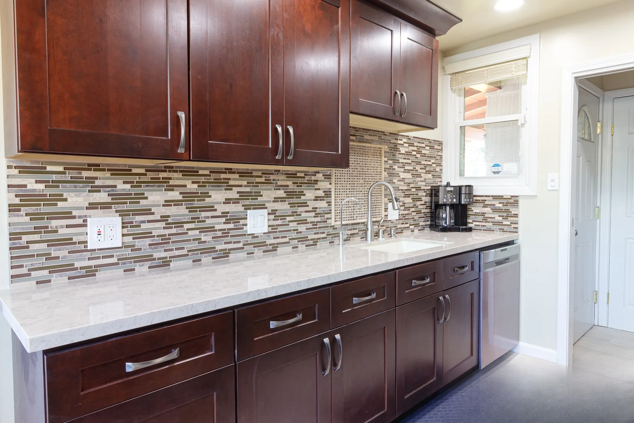 Kitchen after remodel, espresso shaker cabinetry with light quartz counter and glass mosaic backsplash