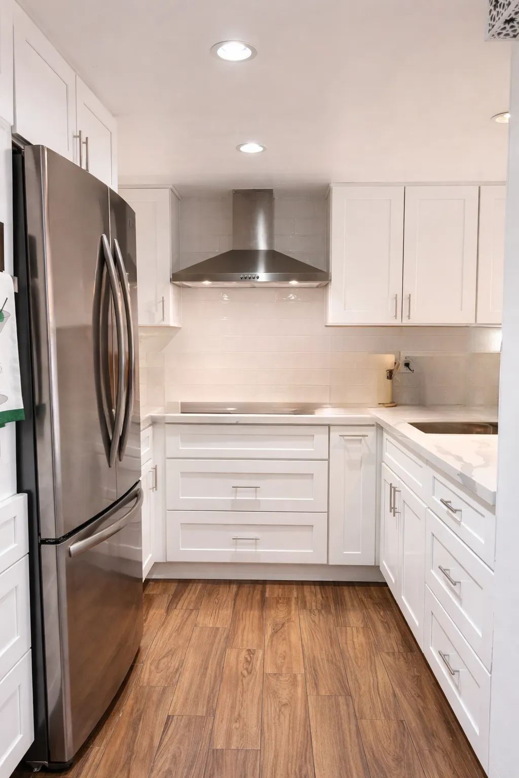 U-shape kitchen after remodel, white shaker cabinetry with light quartz counters and a peninsula with bar seating