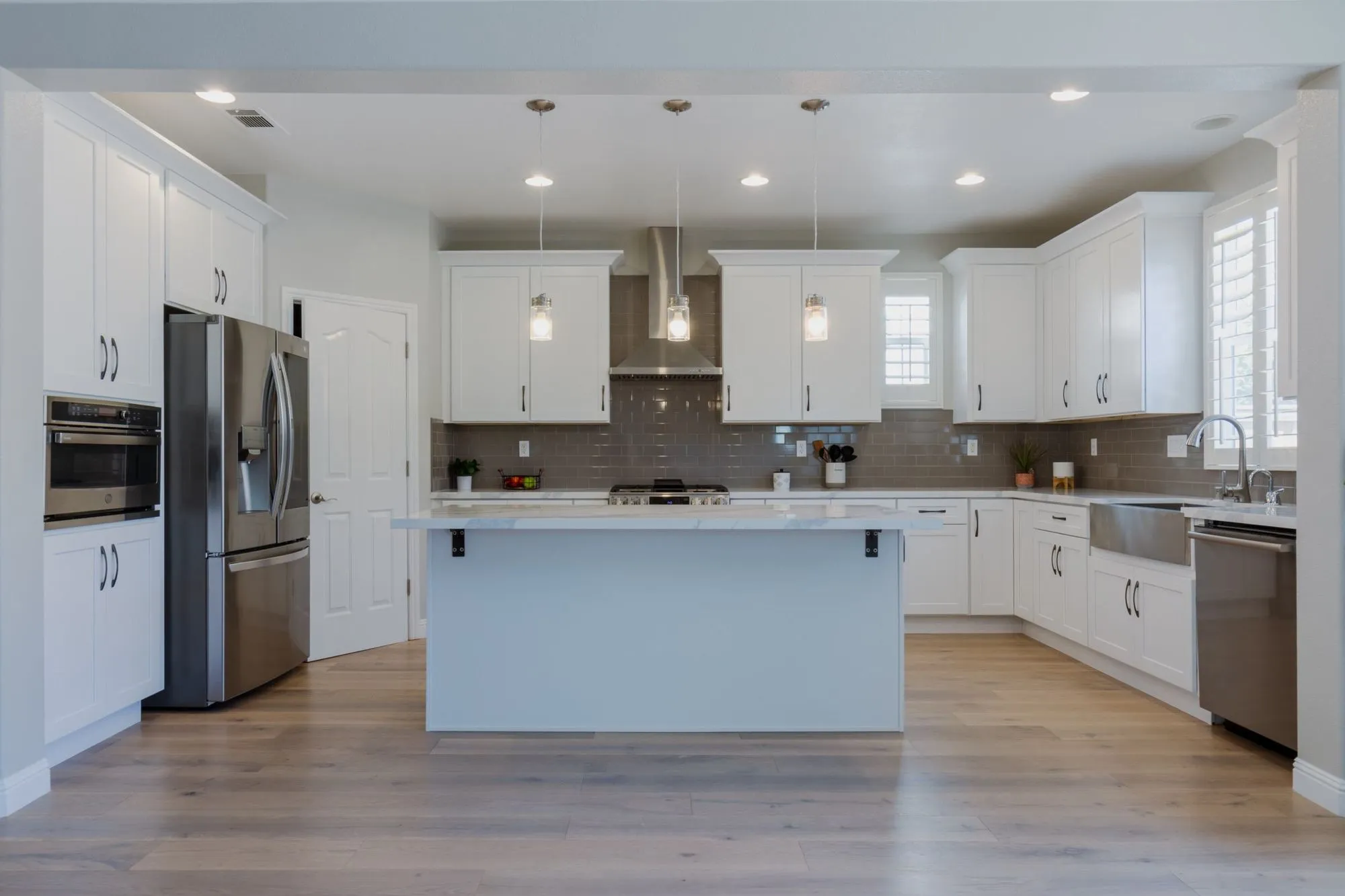 White shaker kitchen after remodel, marble-look quartz island below three glass pendant lights