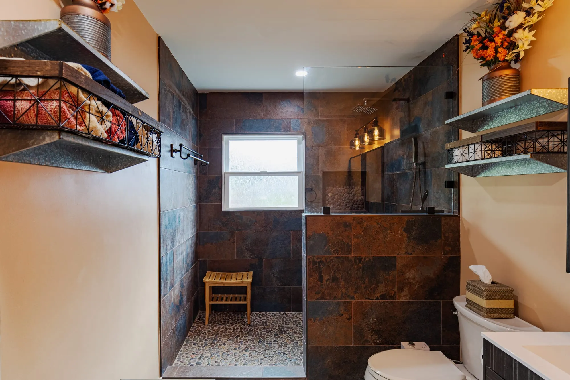 Bathroom after remodel, slate-tone tile shower with a pebble mosaic floor and a teak bench