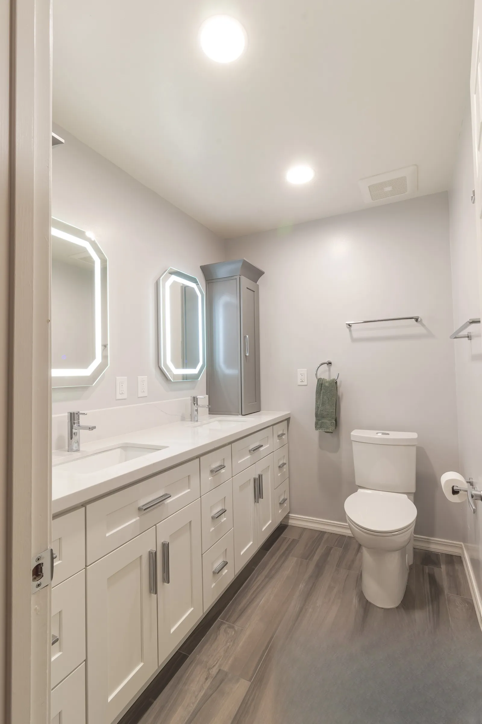 Bathroom after remodel, double vanity with two lit mirrors and wood-look plank tile floor