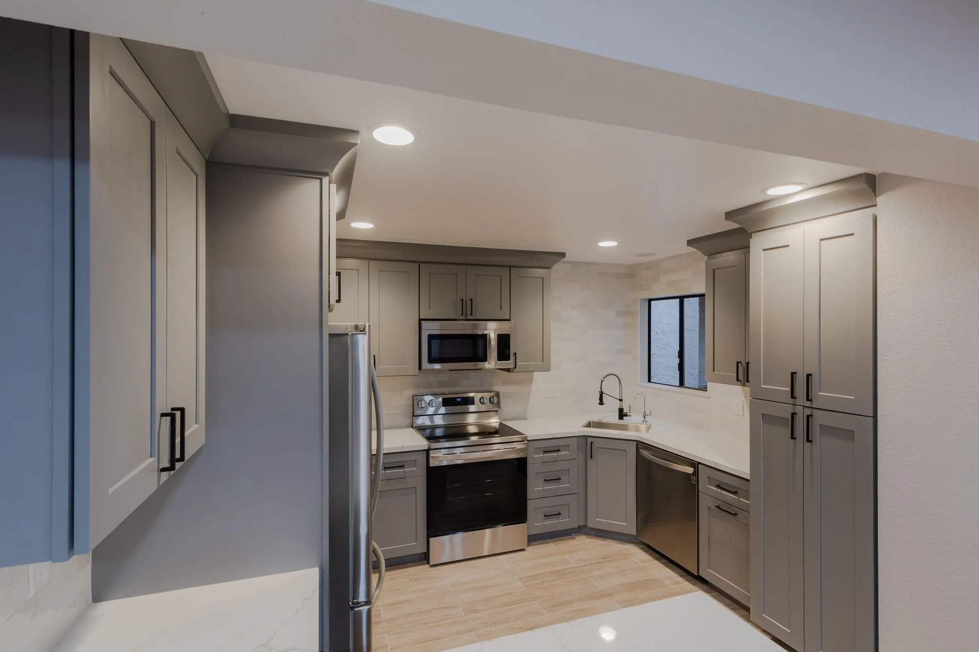 Kitchen after remodel, warm grey shaker cabinetry with quartz counters and a stainless range and refrigerator