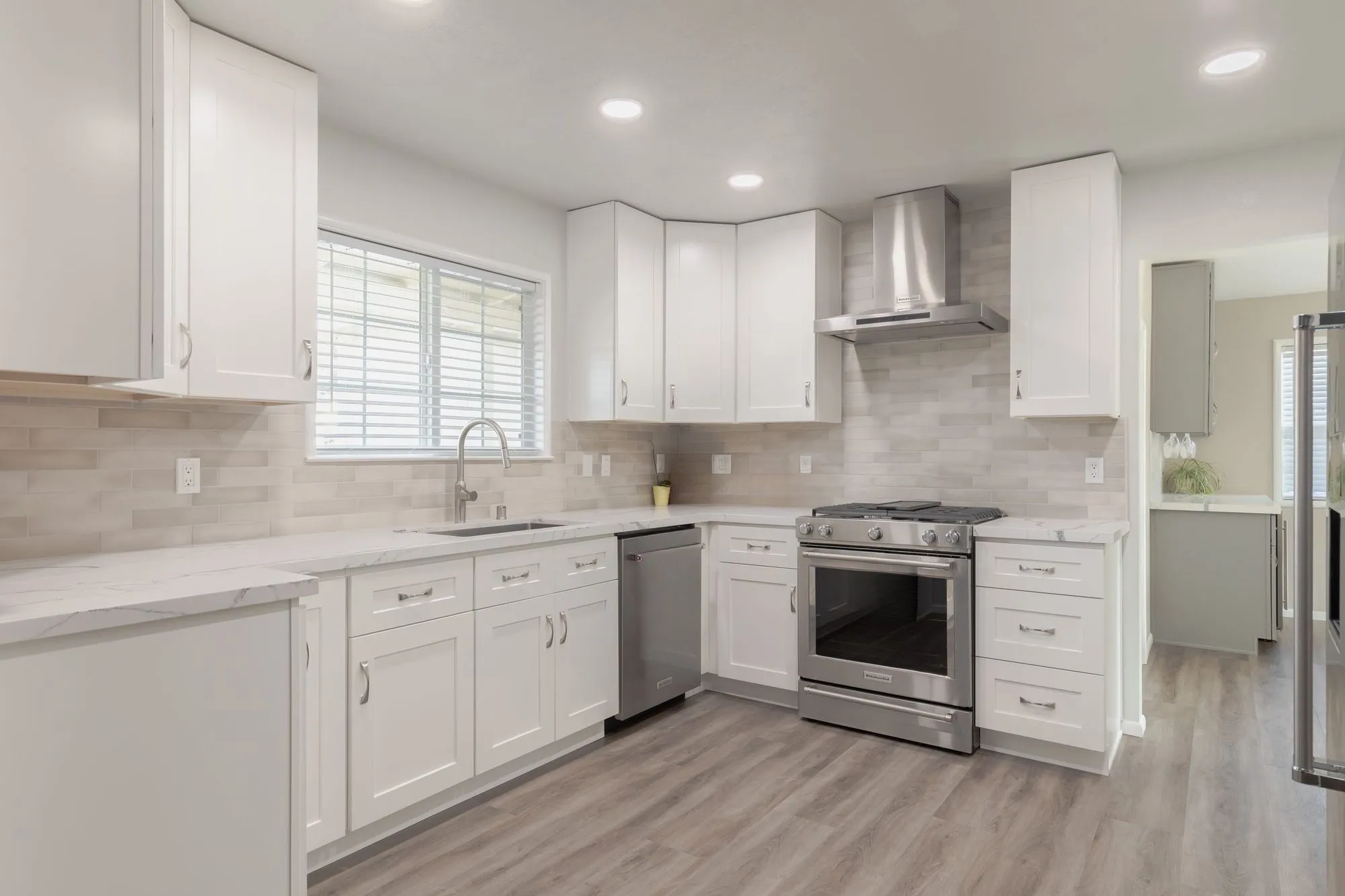 Kitchen after whole-home remodel, white shaker cabinetry with veined quartz counters and a stainless range