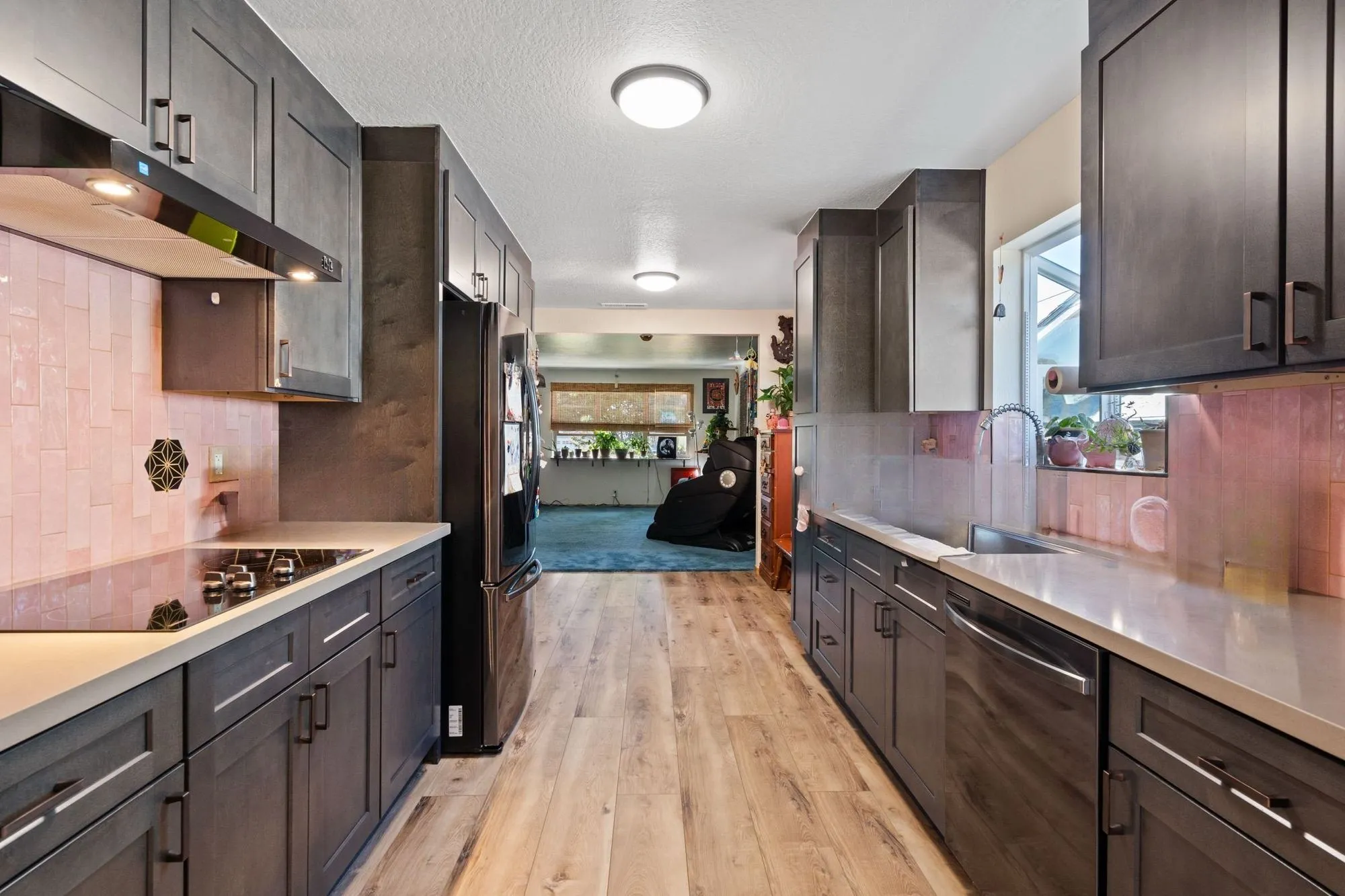 Galley kitchen after whole-home remodel, dark shaker cabinetry and blush tile backsplash with open sightline to living room