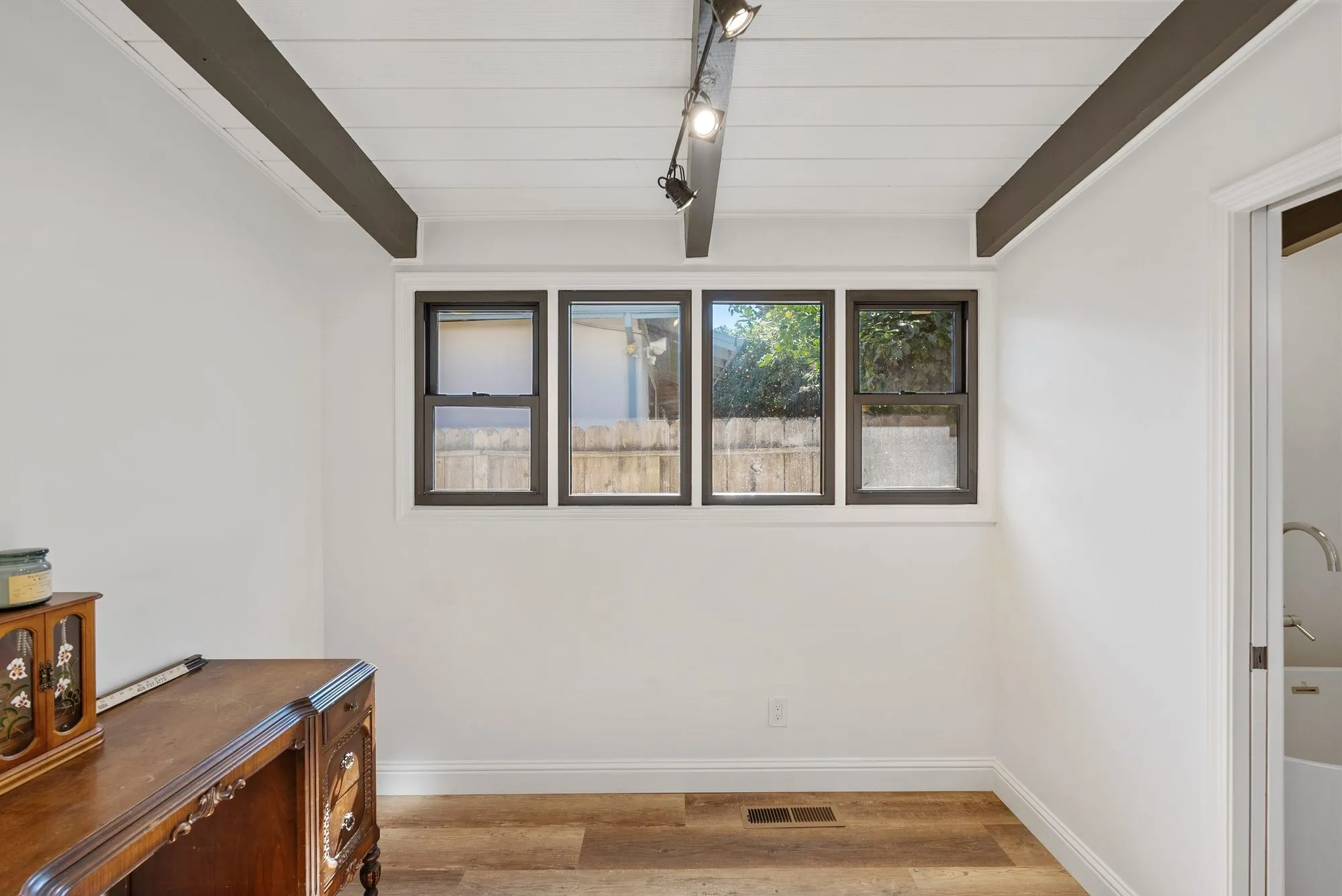 Living space after whole-home remodel, white walls and shiplap ceiling with exposed dark beams, light oak plank flooring and black-framed windows
