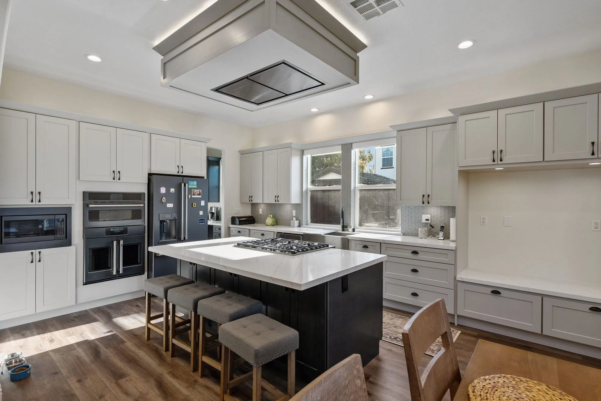 Kitchen after whole-home remodel, white cabinetry with a large island, stacked wall ovens and a flush ceiling hood above the cooktop