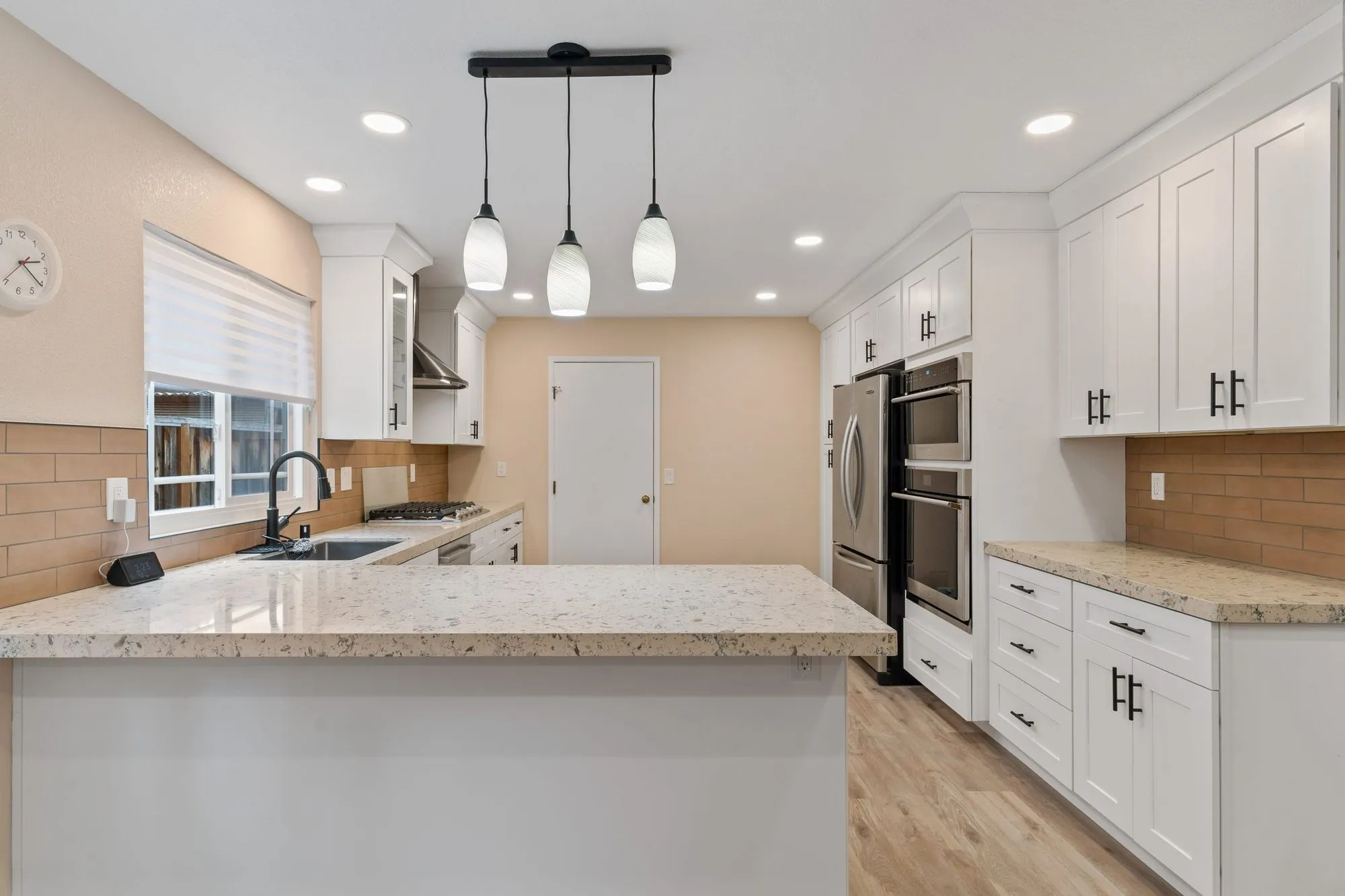 Kitchen after whole-home remodel, white shaker cabinetry with speckled granite counters, tan subway tile backsplash and stacked stainless wall ovens