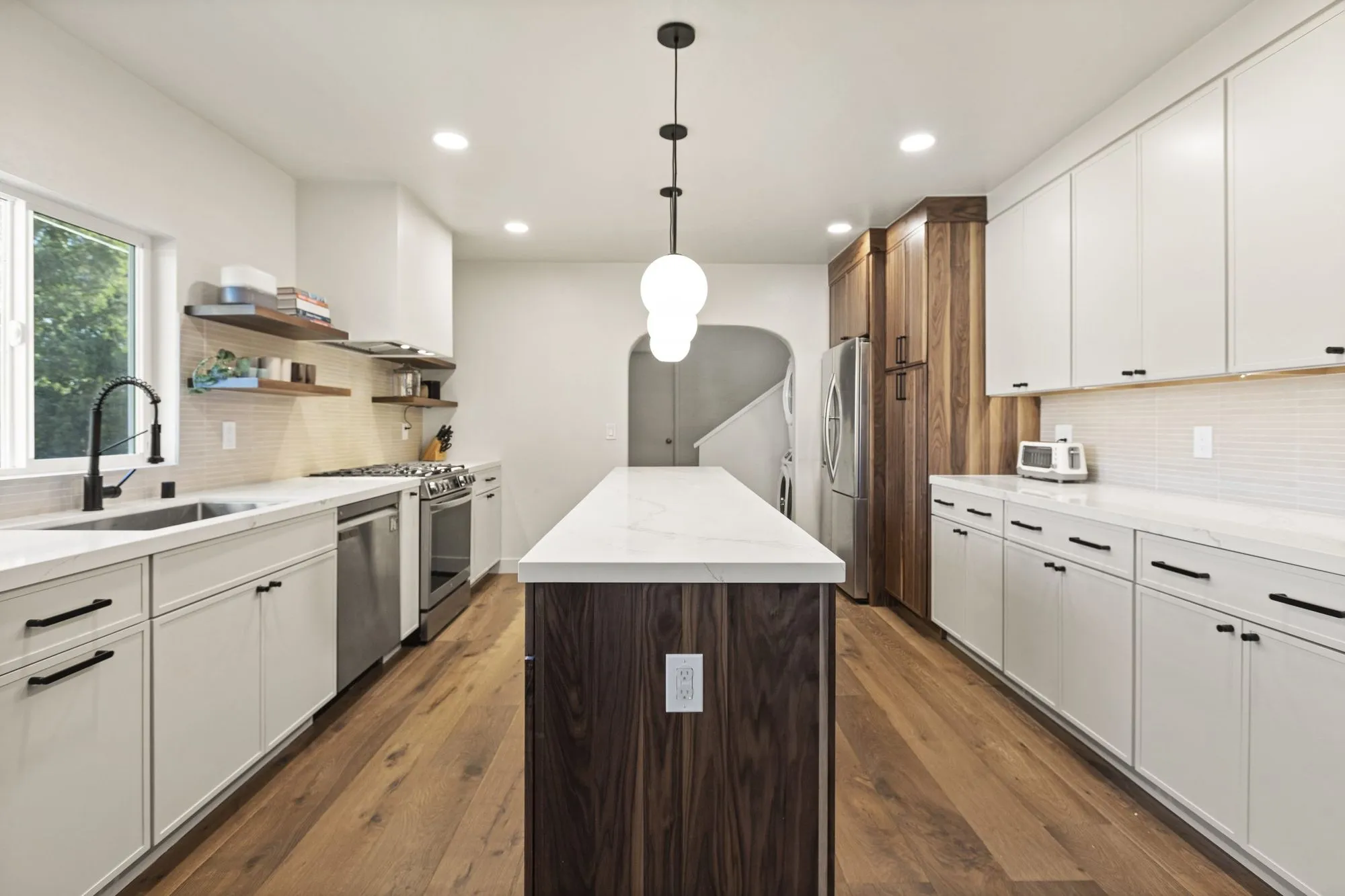 Kitchen after whole-home remodel, white cabinetry with a walnut-fronted island and globe pendant lighting