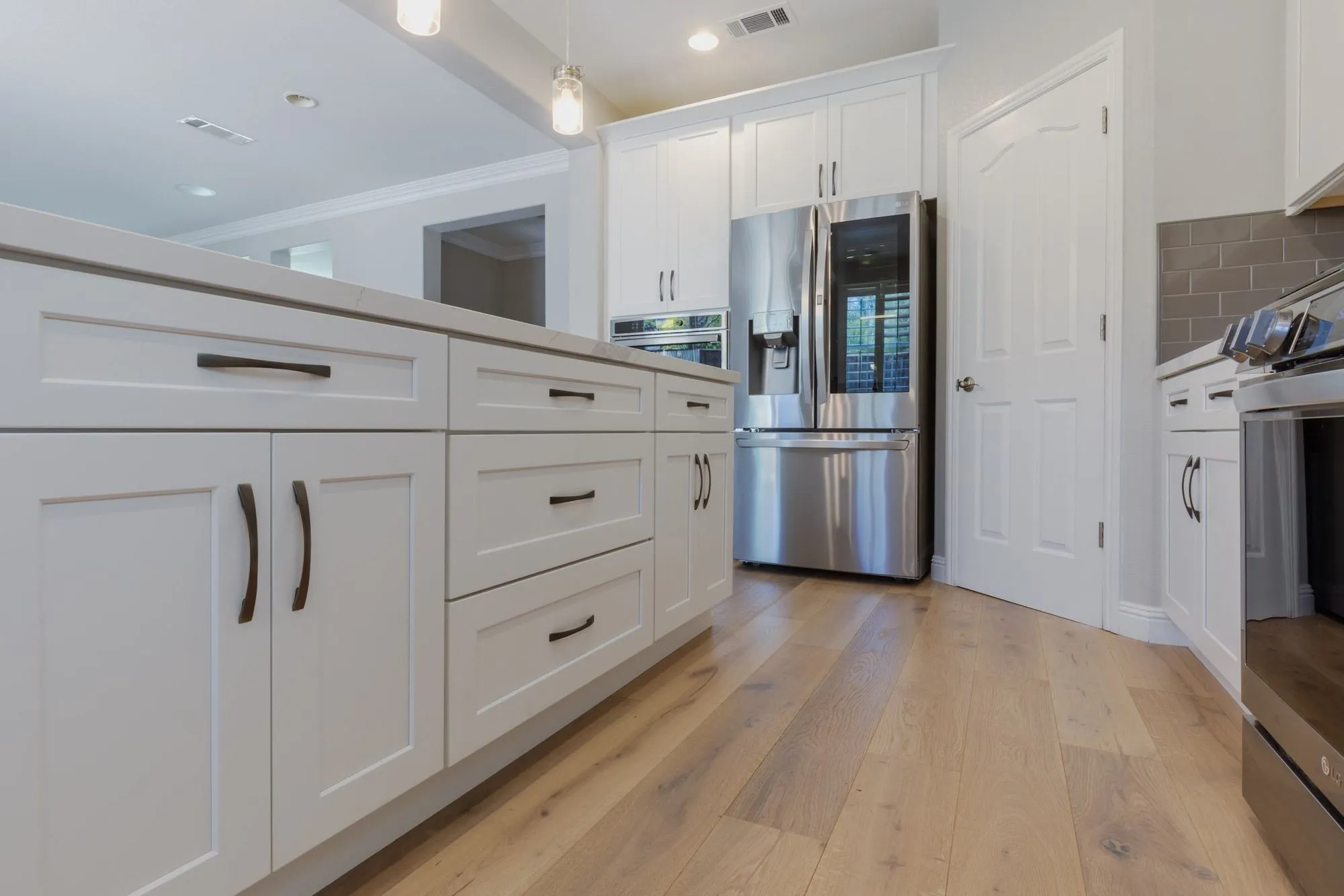Island cabinetry with matte-black pulls above light oak-look plank flooring