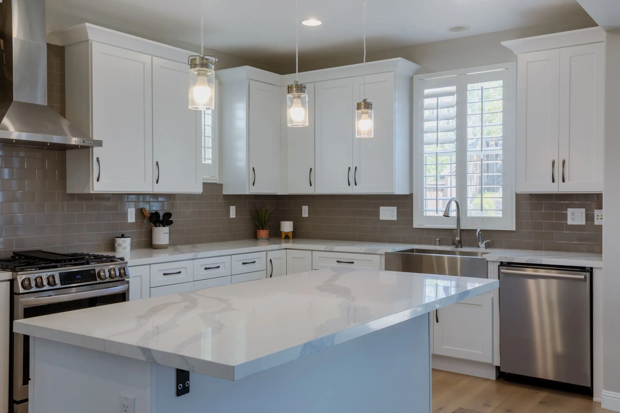Quartz island after remodel, seating on the open side under three glass pendant lights