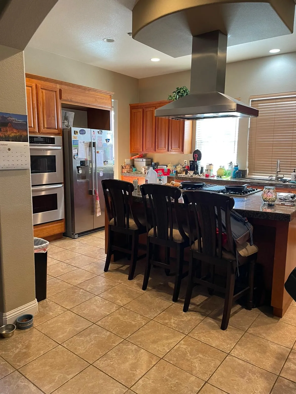 Original kitchen before remodel, honey-oak cabinetry with a tiled island and a stainless canopy hood