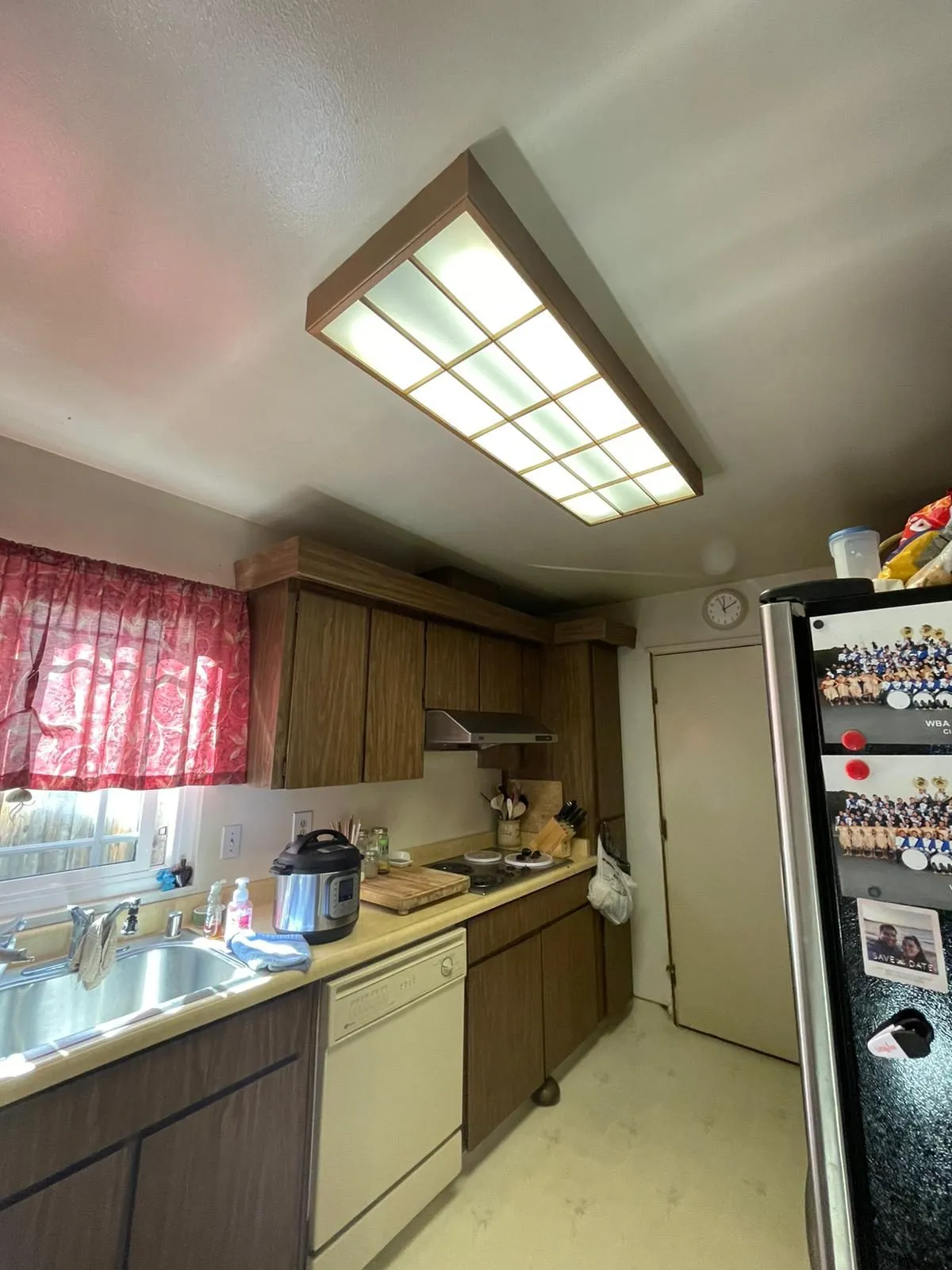 Original kitchen before remodel, dark wood cabinets with laminate counters and a fluorescent ceiling panel