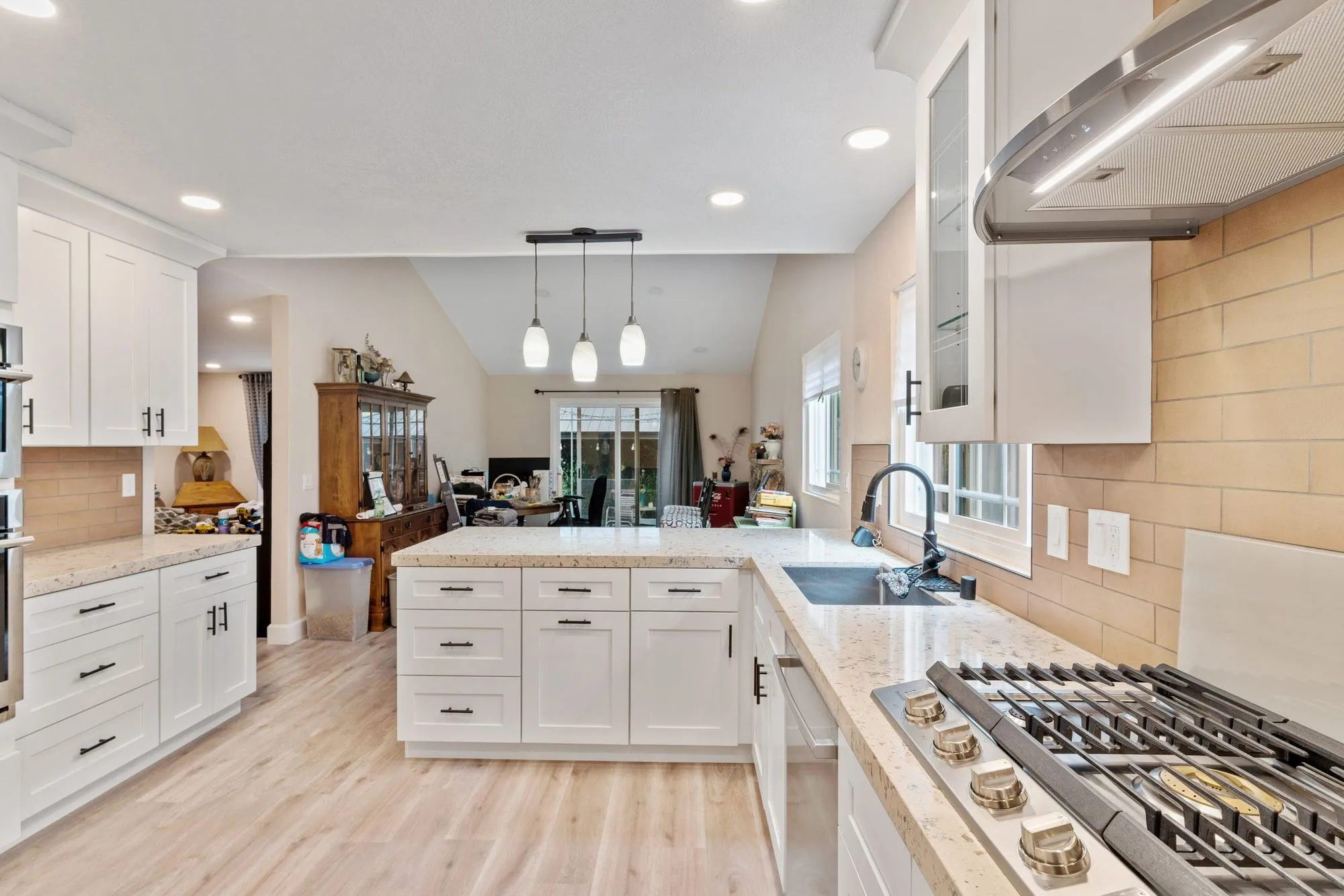 Gas cooktop set into the granite peninsula with the stainless hood above