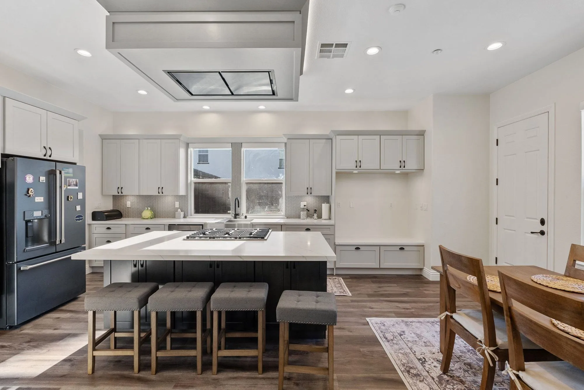 Same kitchen after remodel, white cabinetry with a broad quartz island and bar seating