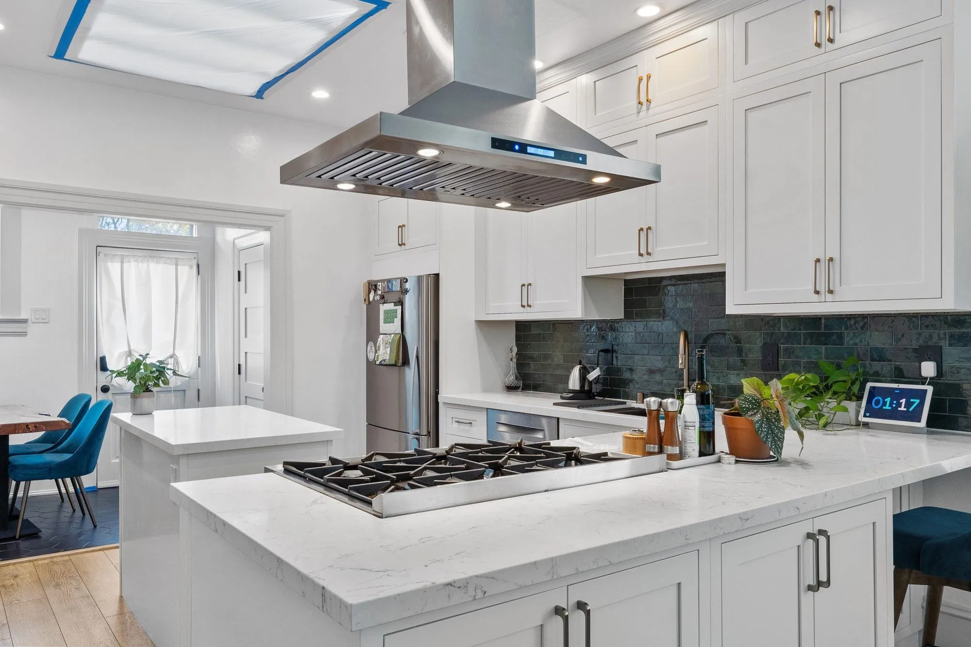 Island cooktop below the stainless hood, open to the dining seating beyond