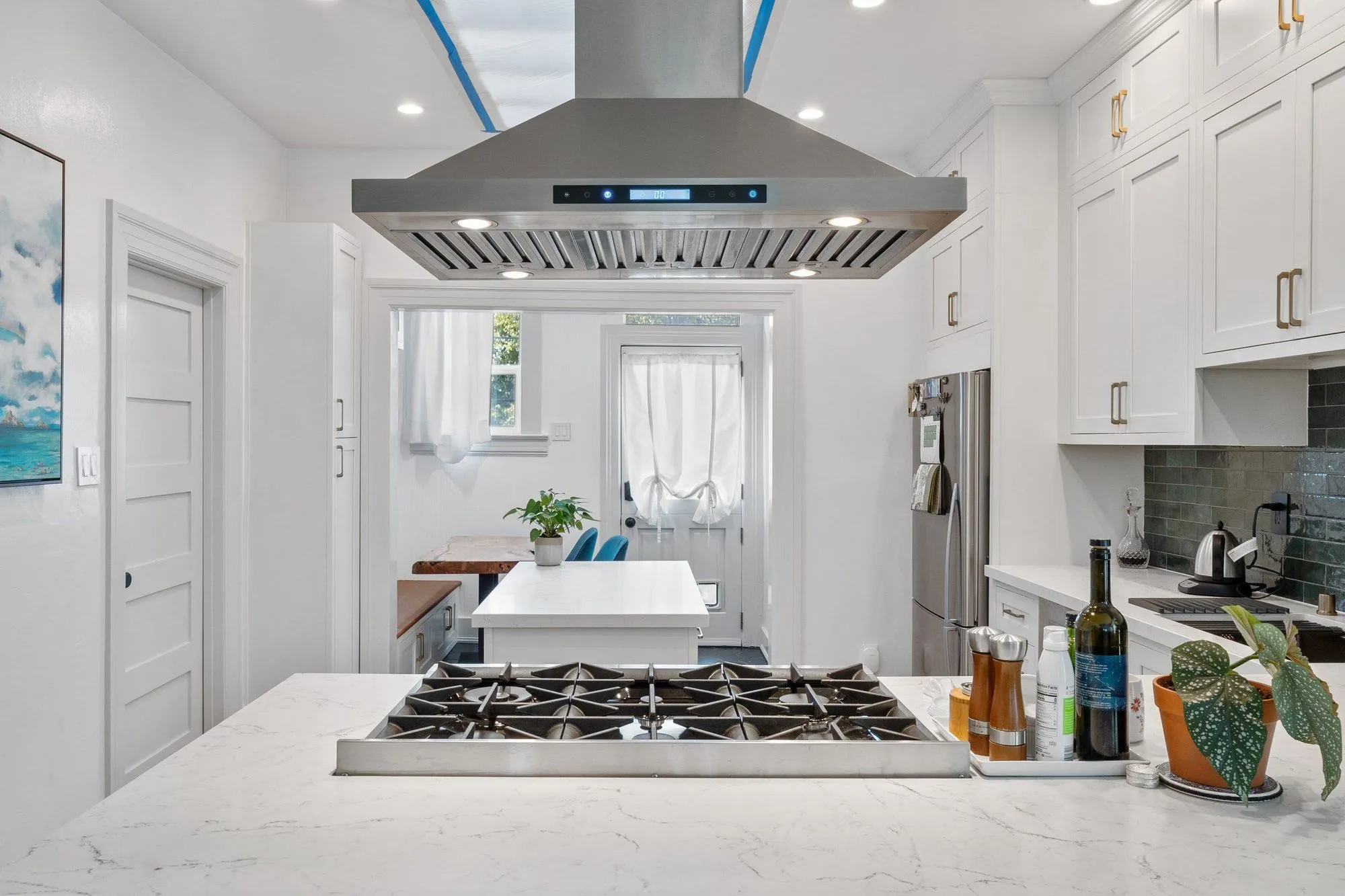 Wide view along the island to the stainless hood suspended above the cooktop
