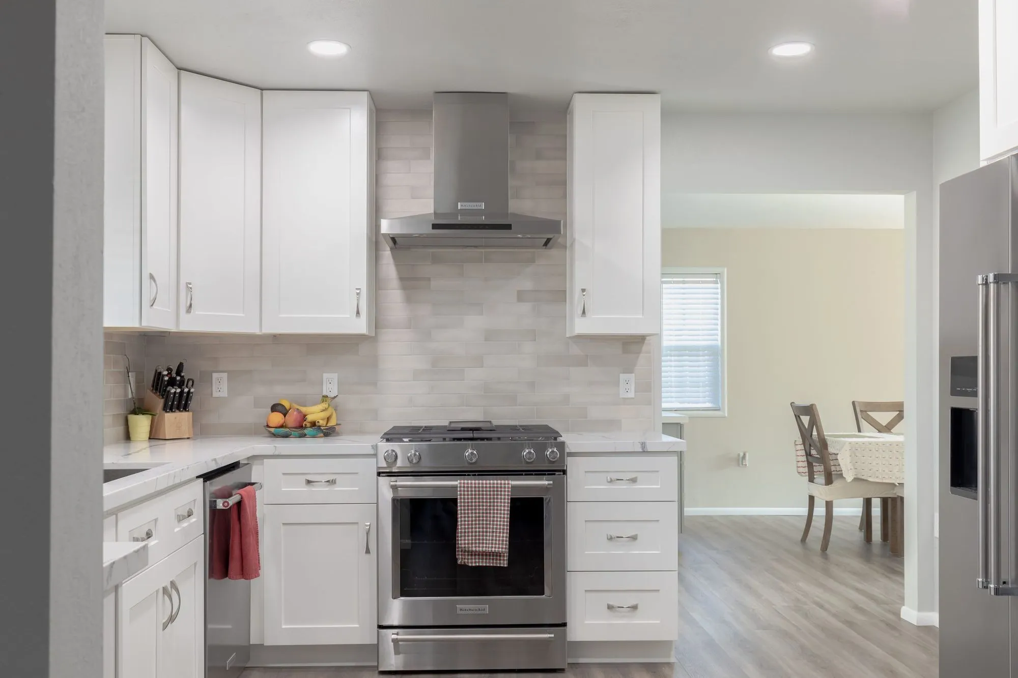 Stainless range under a wall-mounted hood, looking through to the dining area beyond