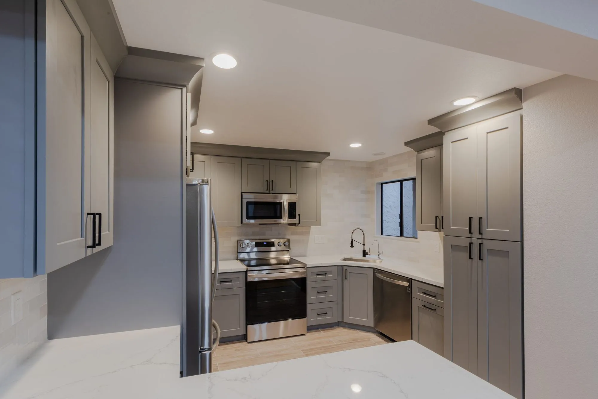 Stainless range and microwave set into the warm grey cabinetry run below quartz counters