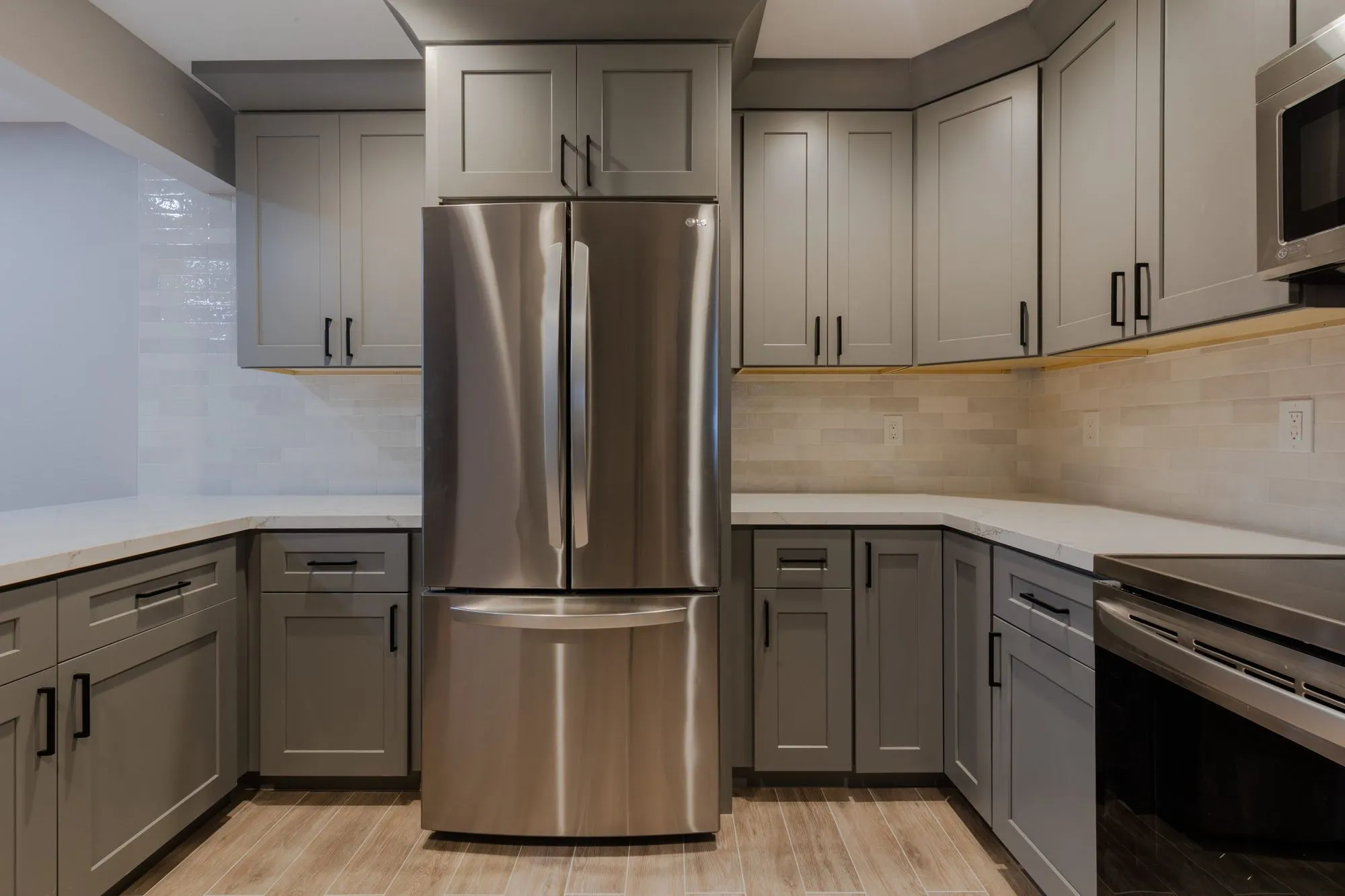 Stainless refrigerator beside the counter run in warm grey shaker cabinetry