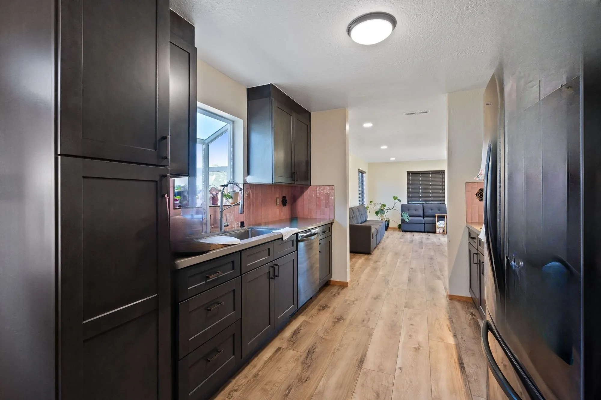 Same galley kitchen after remodel, dark shaker cabinetry and plank flooring with open sightline