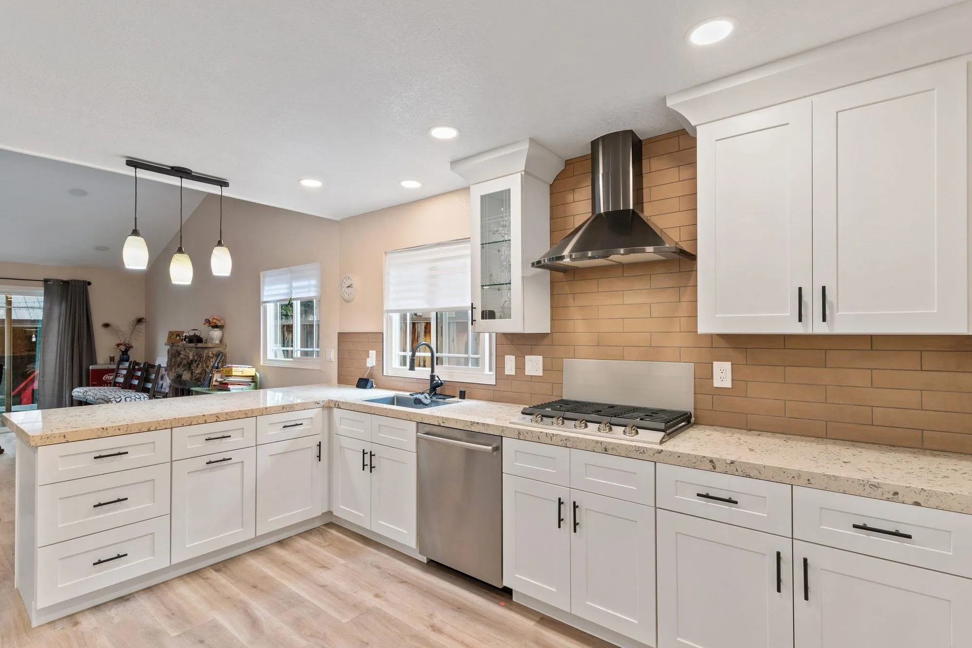 Same kitchen after remodel, white shaker cabinetry in a U-shape with granite counters and a stainless range hood