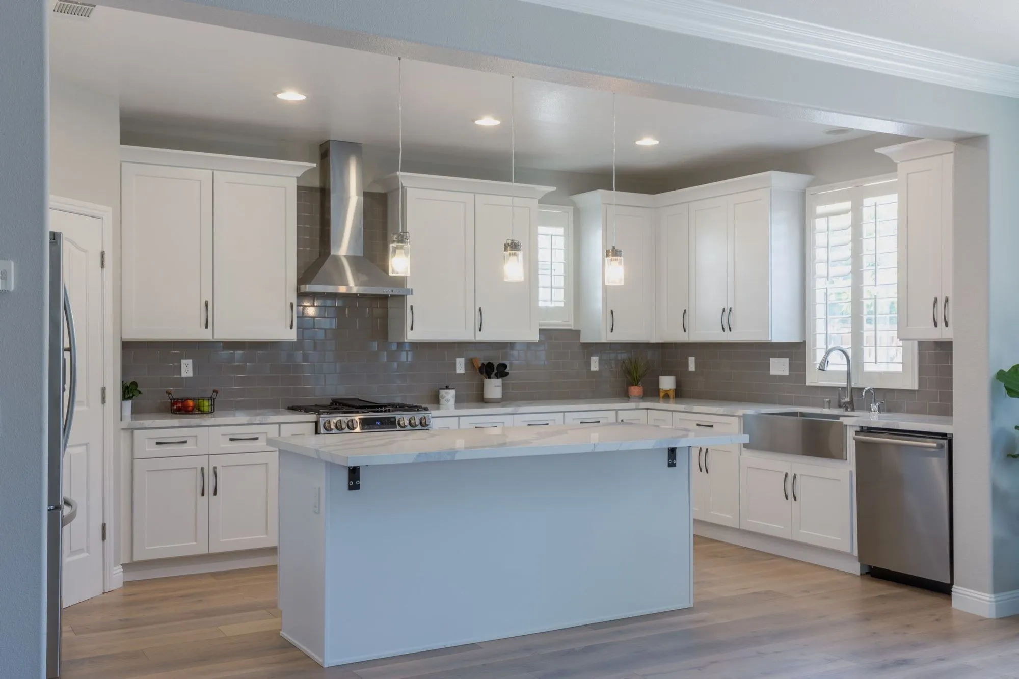 Kitchen after remodel, white shaker cabinetry with stainless chimney hood and grey subway tile