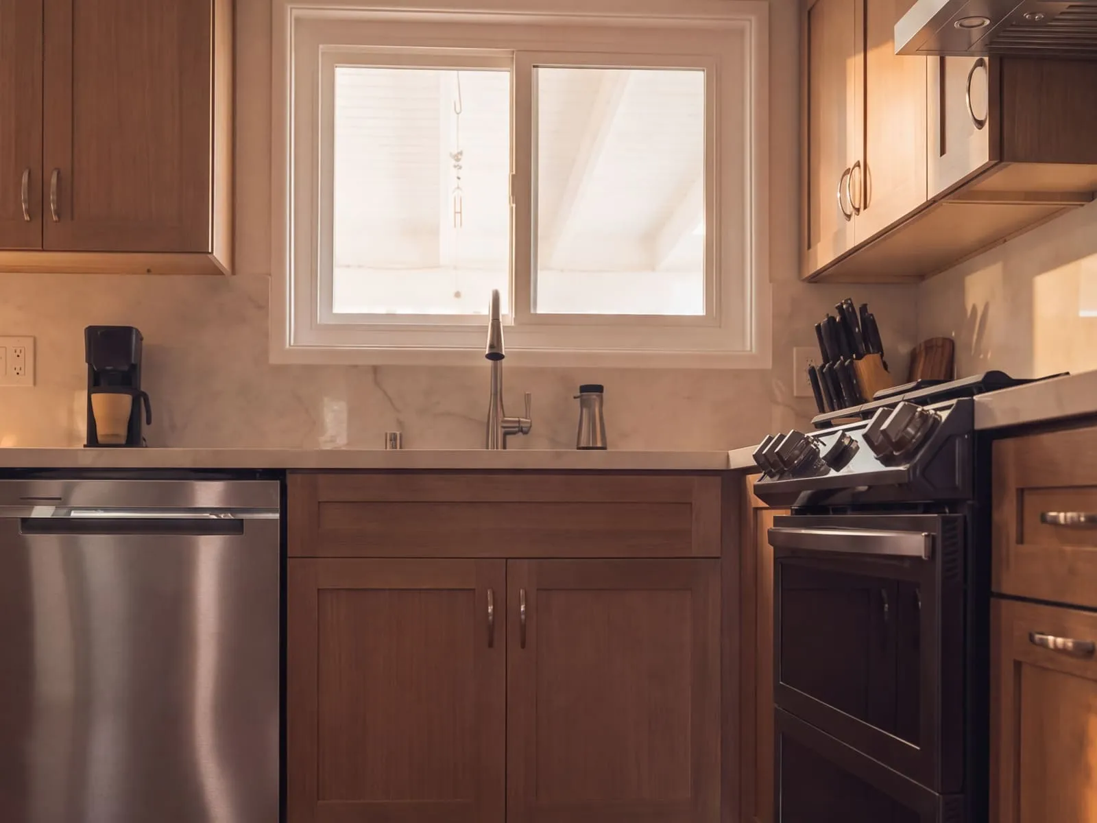 Undermount sink below the window between the dishwasher and the range, under wood shaker upper cabinets
